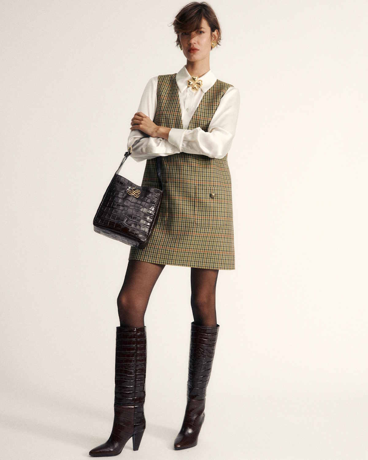 Modelka w eleganckiej sukience w kratkę, białej koszuli i długich, ciemnych kozakach, trzyma torebkę. Luisa Spagnoli Kolekcja Pre Fall 2025.