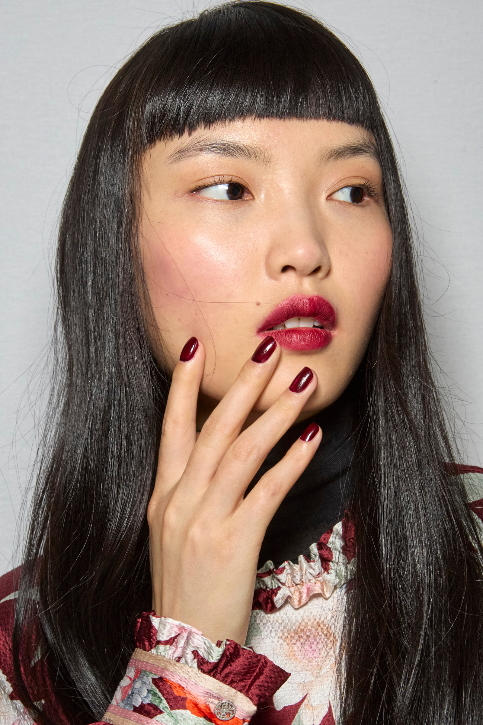 Ciemnoczerwony lakier na paznokciach, manicure w kolorze cherry red, oraz zaręczynowy pierścionek na dłoni modelki.