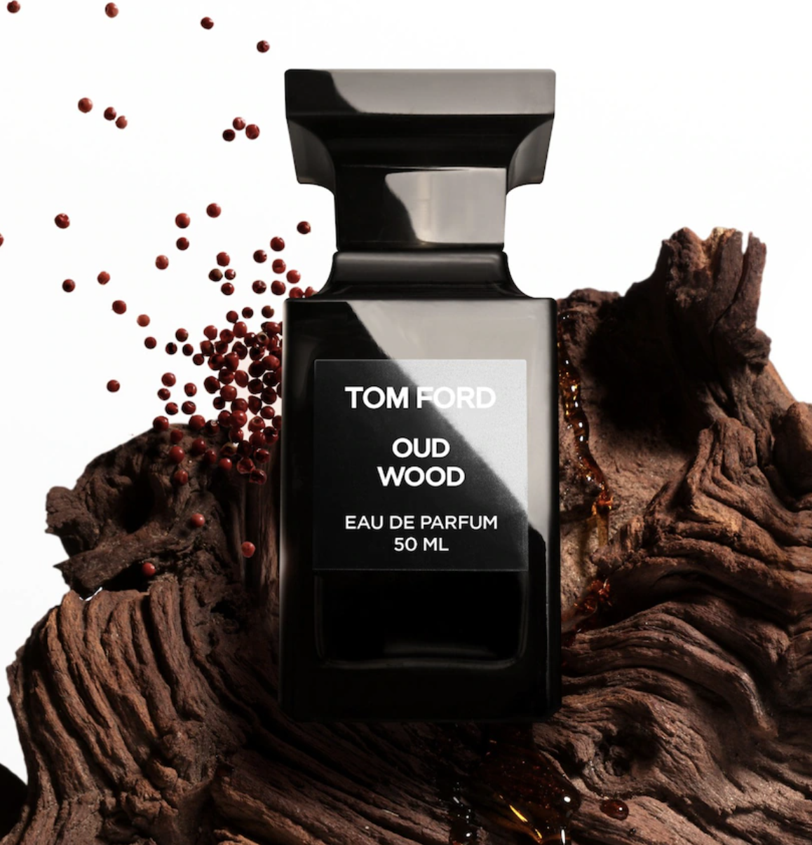 Perfumy na jesień w eleganckiej butelce Tom Ford Oud Wood, otoczone drewnem i drobnymi kulkami.