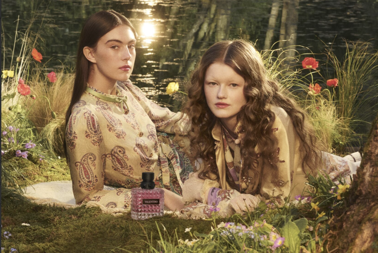 Dwie kobiety w ubraniach w stylu vintage, otoczone naturą, pozują z butelką perfum na jesień Valentino.
