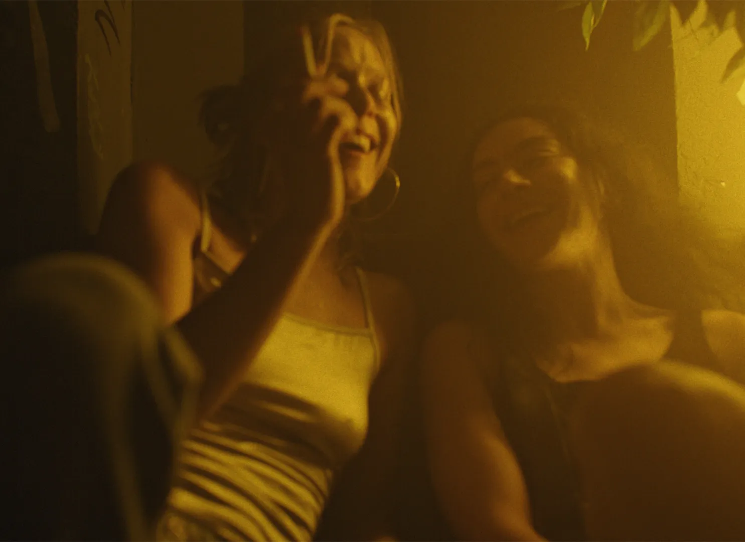 Kadr z filmu "Erupcja", w którym Lena Góra i Charli XCX bawią się w ciepłym, przytłumionym świetle.