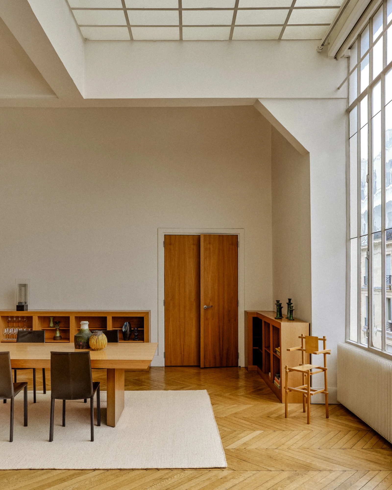 Jasne wnętrze z dużymi oknami, sosnowe meble oraz stół z krzesłami w minimalistycznym stylu.