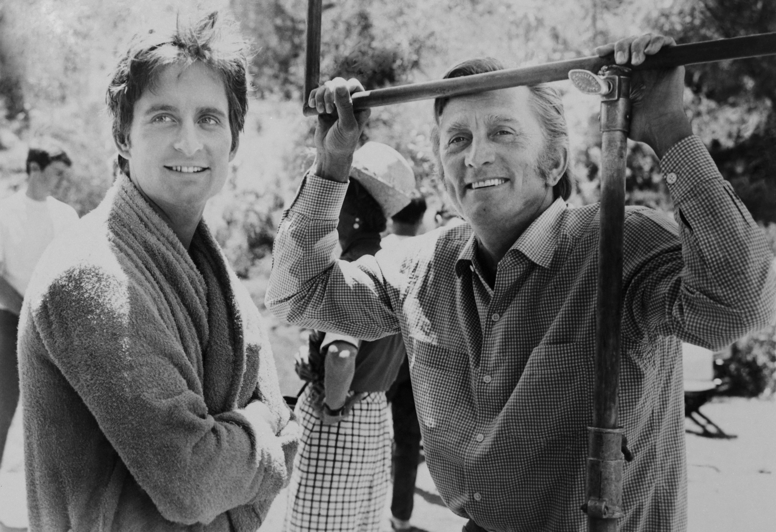 Michael Douglas i Kirk Douglas na planie filmowym, uśmiechnięci i zrelaksowani w otoczeniu przyrody.