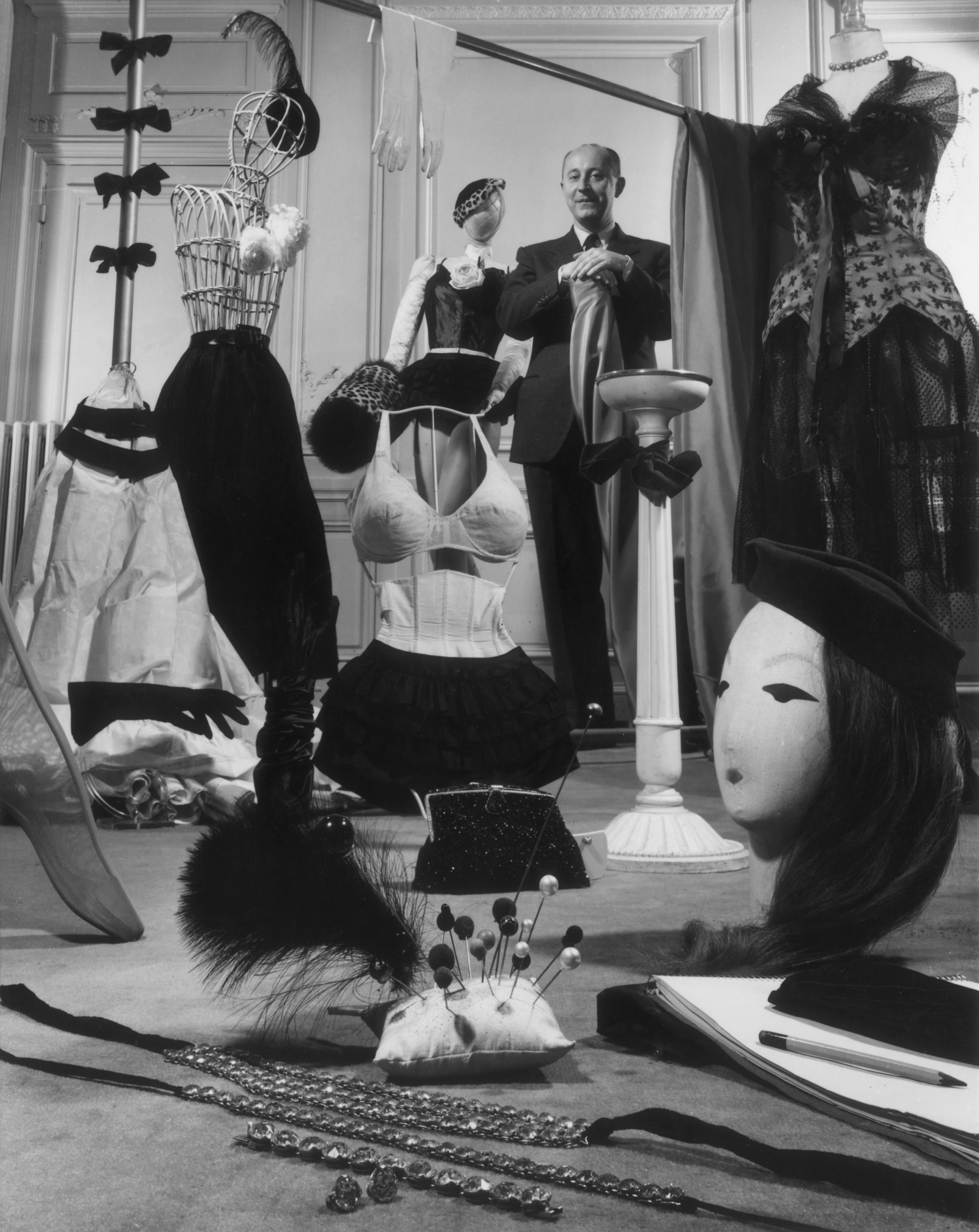 Christian Dior stoi w otoczeniu manekinów i akcesoriów modowych, w eleganckim wnętrzu.