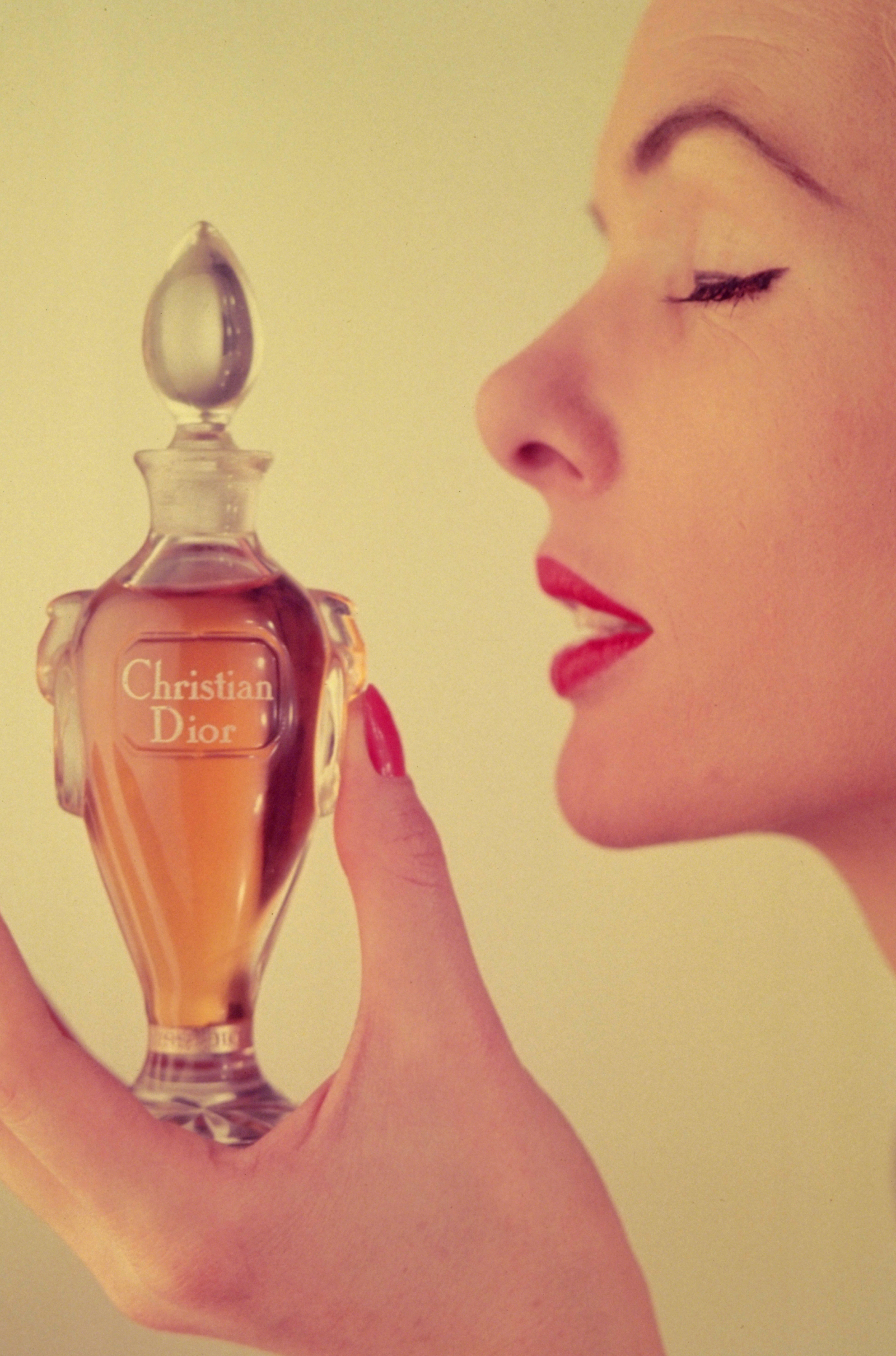 Kobieta trzymająca butelkę perfum Miss Dior, z wyczekiwaną miną, w tle delikatne kolory reklamy.