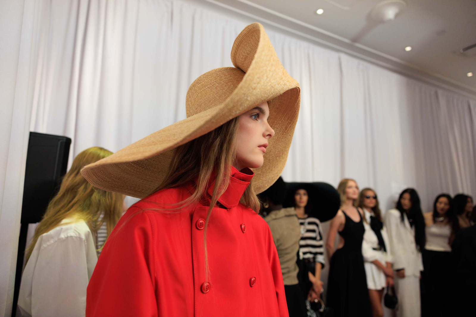 Backstage pokazu Ralph Lauren wiosna 2026, modelka w czerwonym płaszczu i dużym kapeluszu.