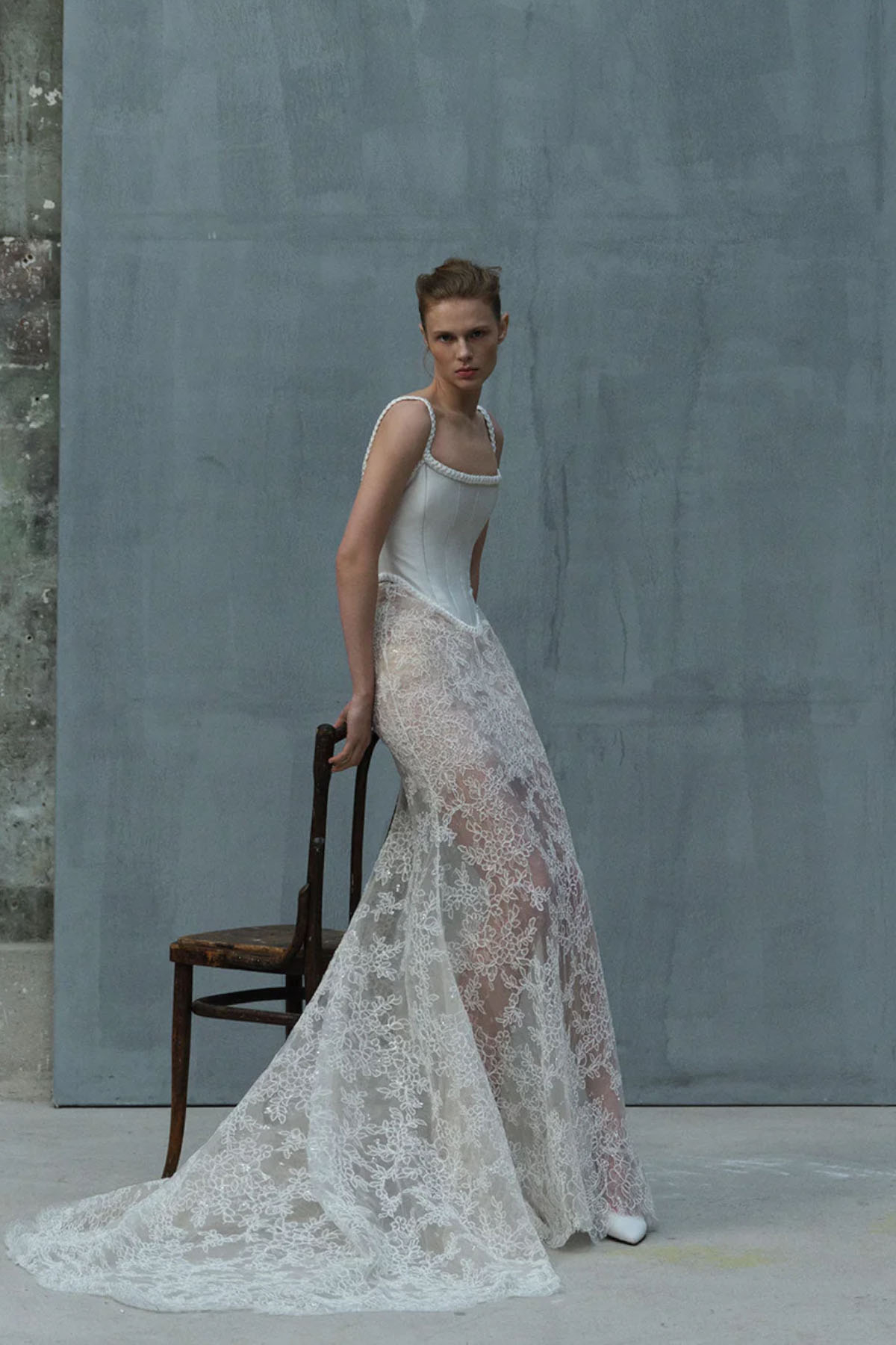 Modelka w eleganckiej sukni projektu Elie Saab, z koronkowym dołem i stylowym gorsetem, siedząca na drewnianym krześle.