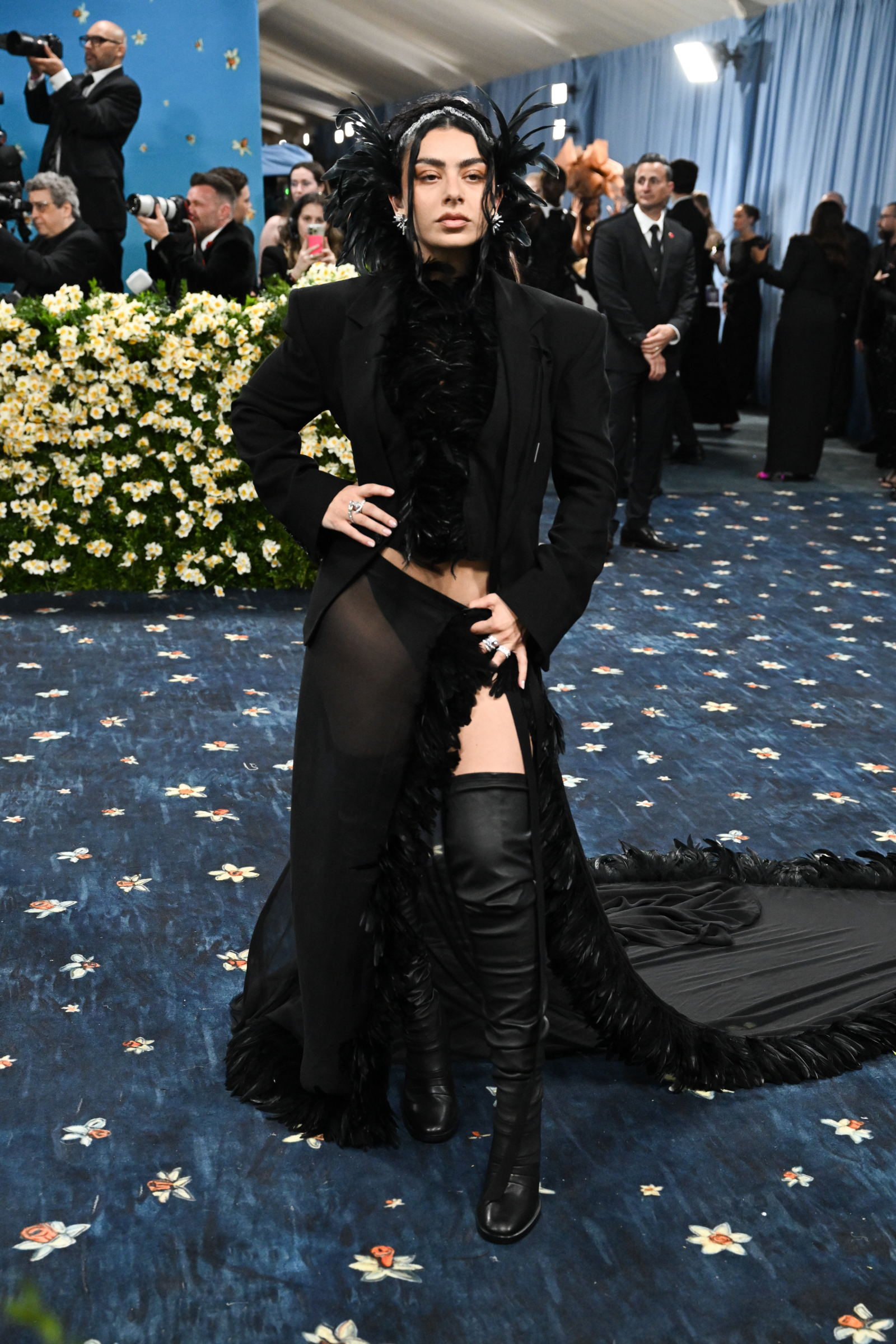 Charli XCX w odważnej stylizacji na Met Gala 2025, z czarnym futrem i wysokimi butami, pozując na czerwonym dywanie.