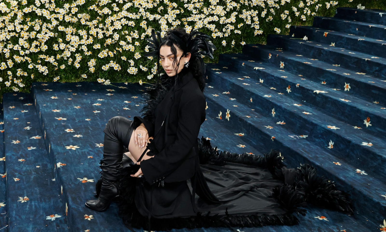 Charli XCX w eleganckiej kreacji na schodach podczas Met Gala 2025, otoczona białymi kwiatami.
