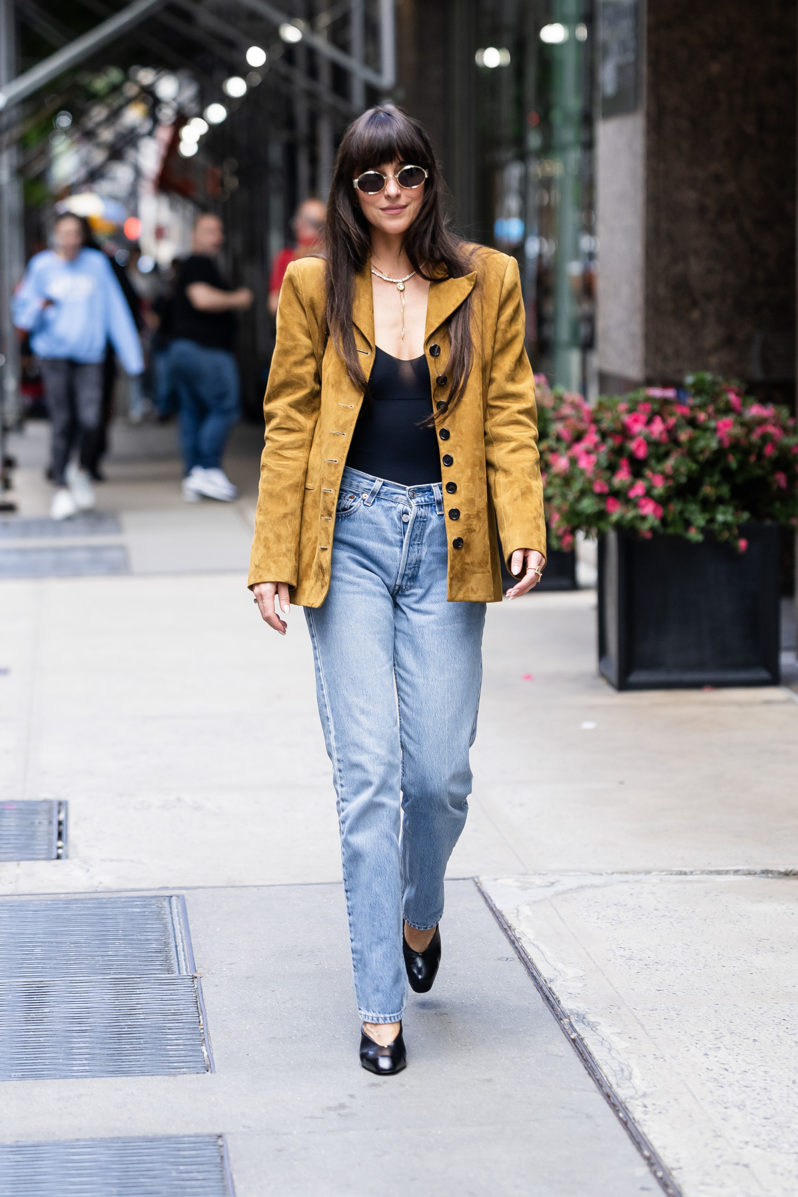 Dakota Johnson w prostych niebieskich jeansach, body i zamszowej marynarce, spaceruje po ulicy.
