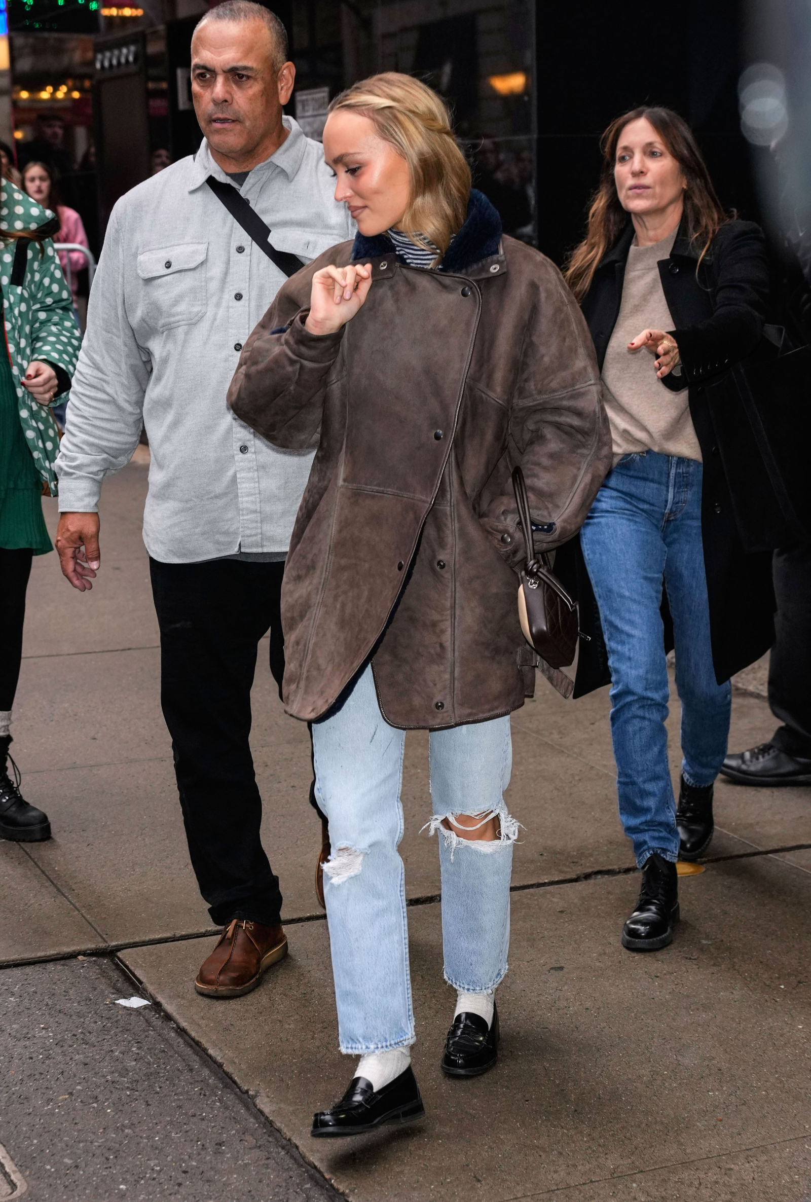 Lily-Rose Depp w jeansach z dziurami, spaceruje w towarzystwie dwóch osób na ulicy.