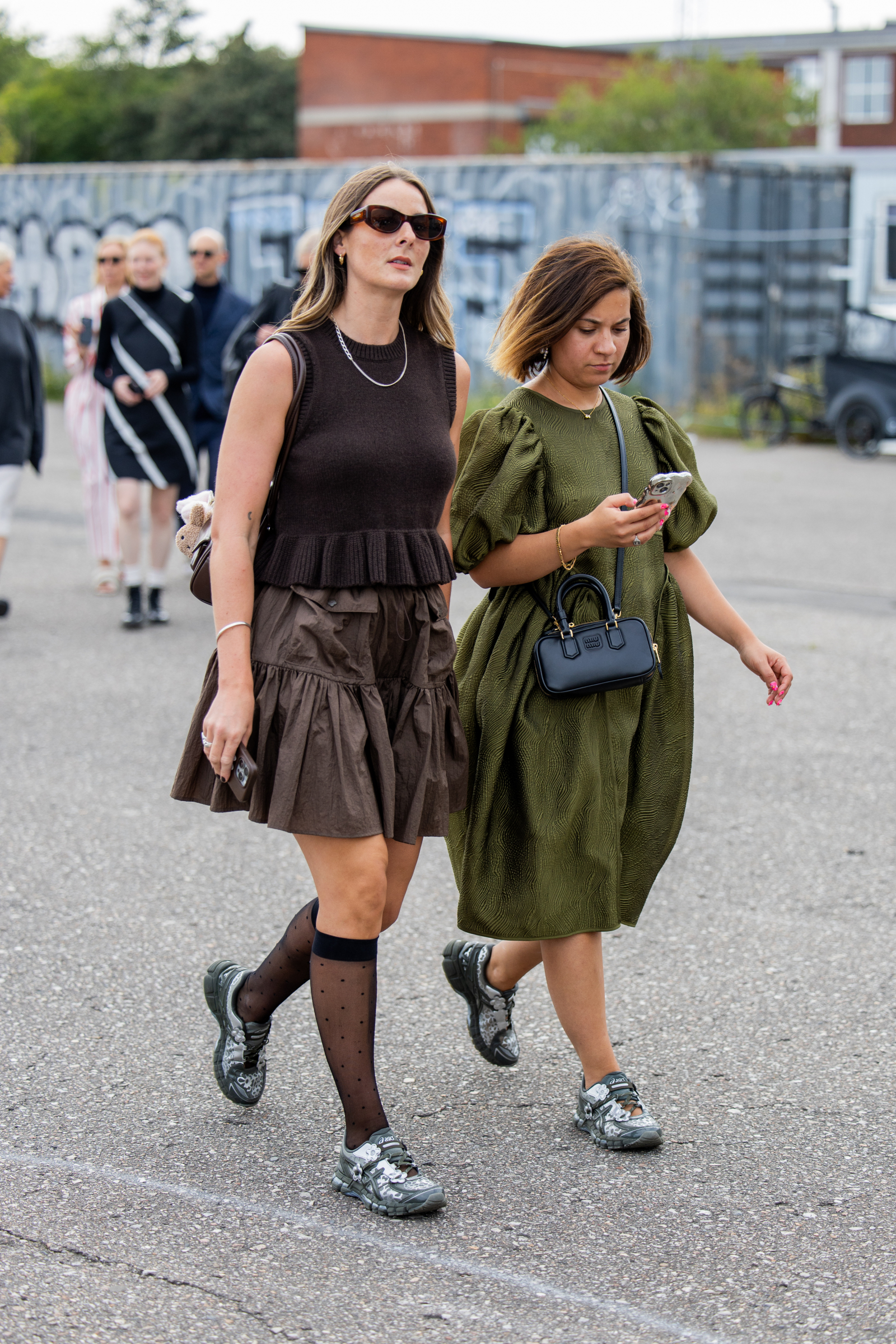 Dwie kobiety spacerują w Kopenhadze w eleganckich stylizacjach, obie w sneakersach Asics x Cecilie Bahnsen.