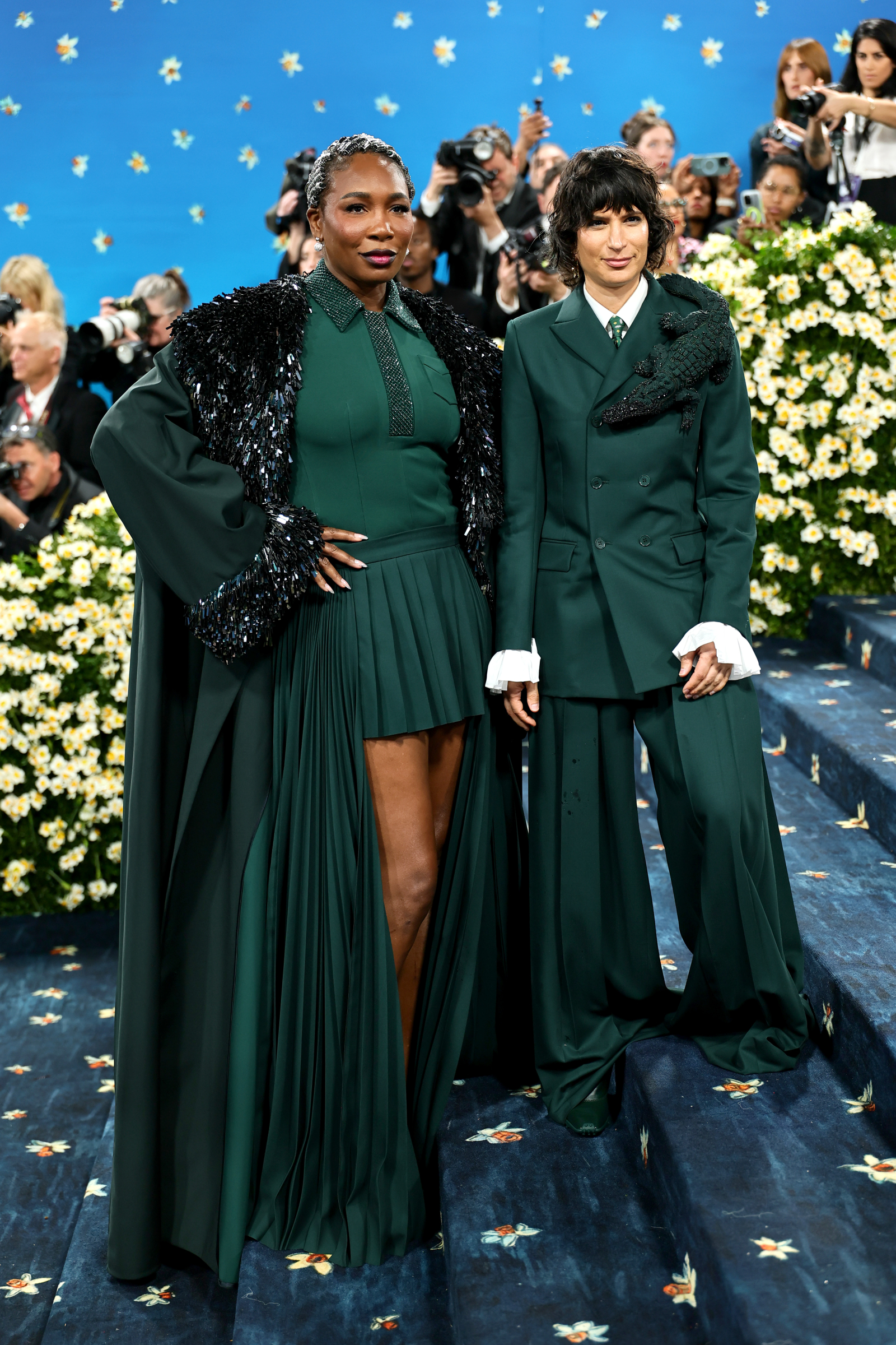 Venus Williams na Met Gala 2025 w stylizacji w zielonym kolorze, pozująca z towarzyszką na schodach otoczonych kwiatami.