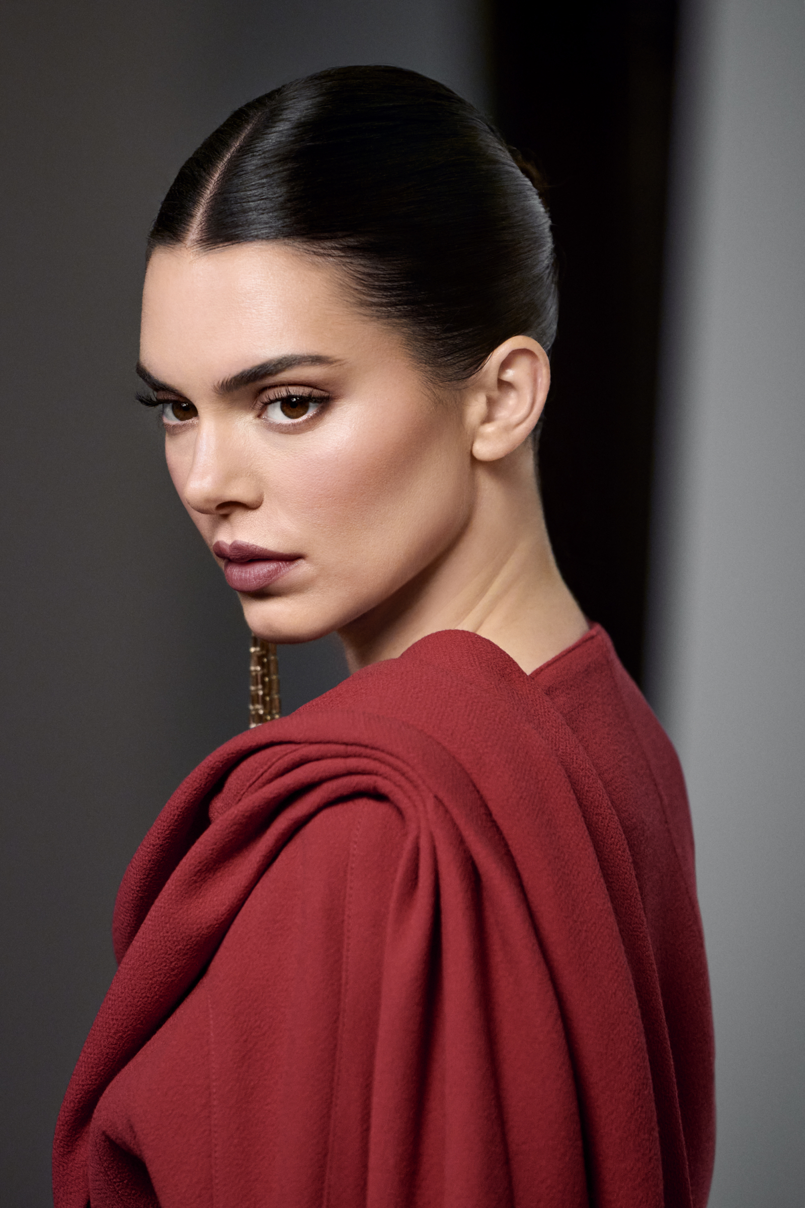 Kendall Jenner w eleganckiej, czerwonej sukni z efektownymi detalami, patrzy w stronę obiektywu.