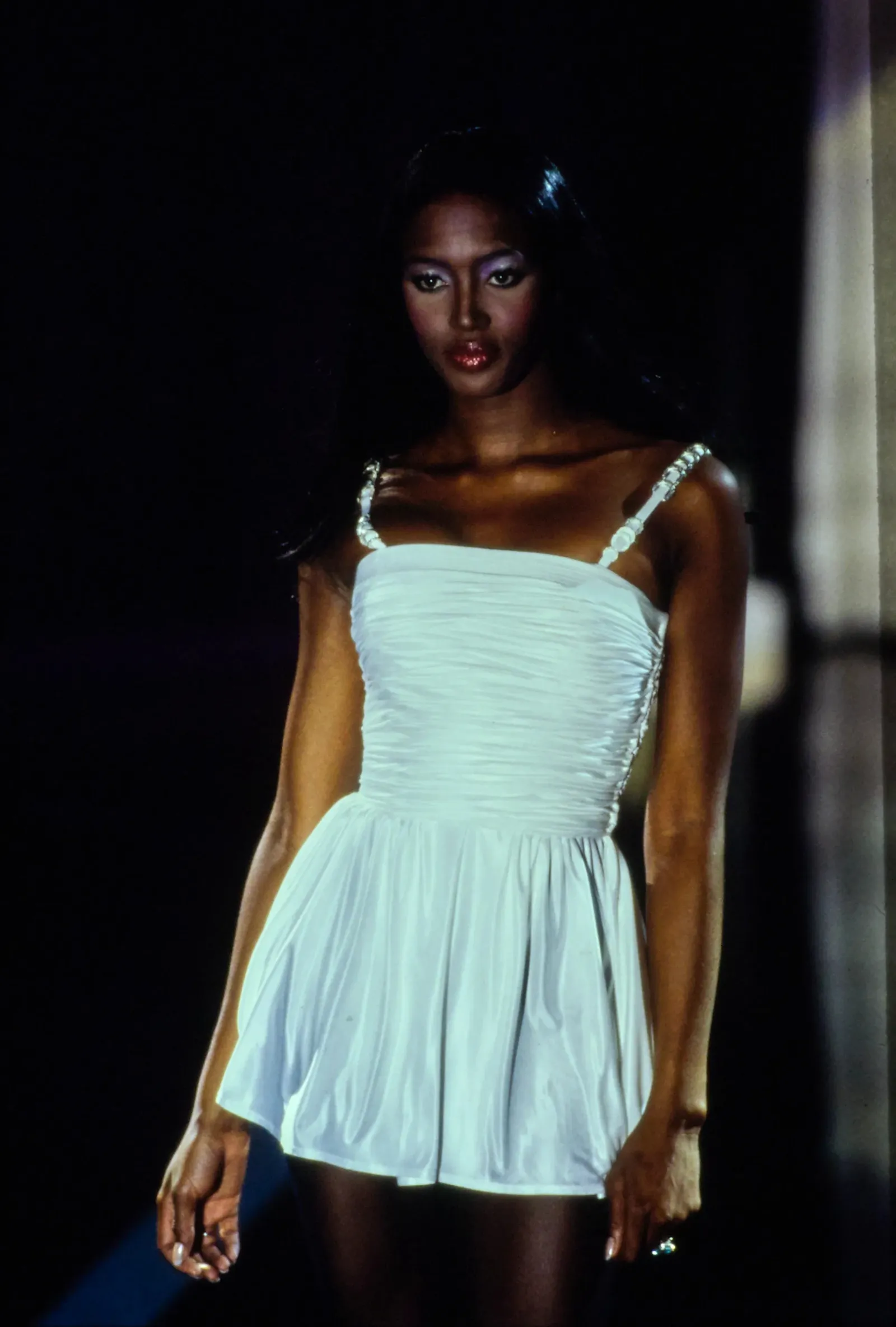 Na wybiegu modelka prezentuje białą minisukienkę Versace z 1993 roku, o wyjątkowym kroju i detalu na ramiączkach.