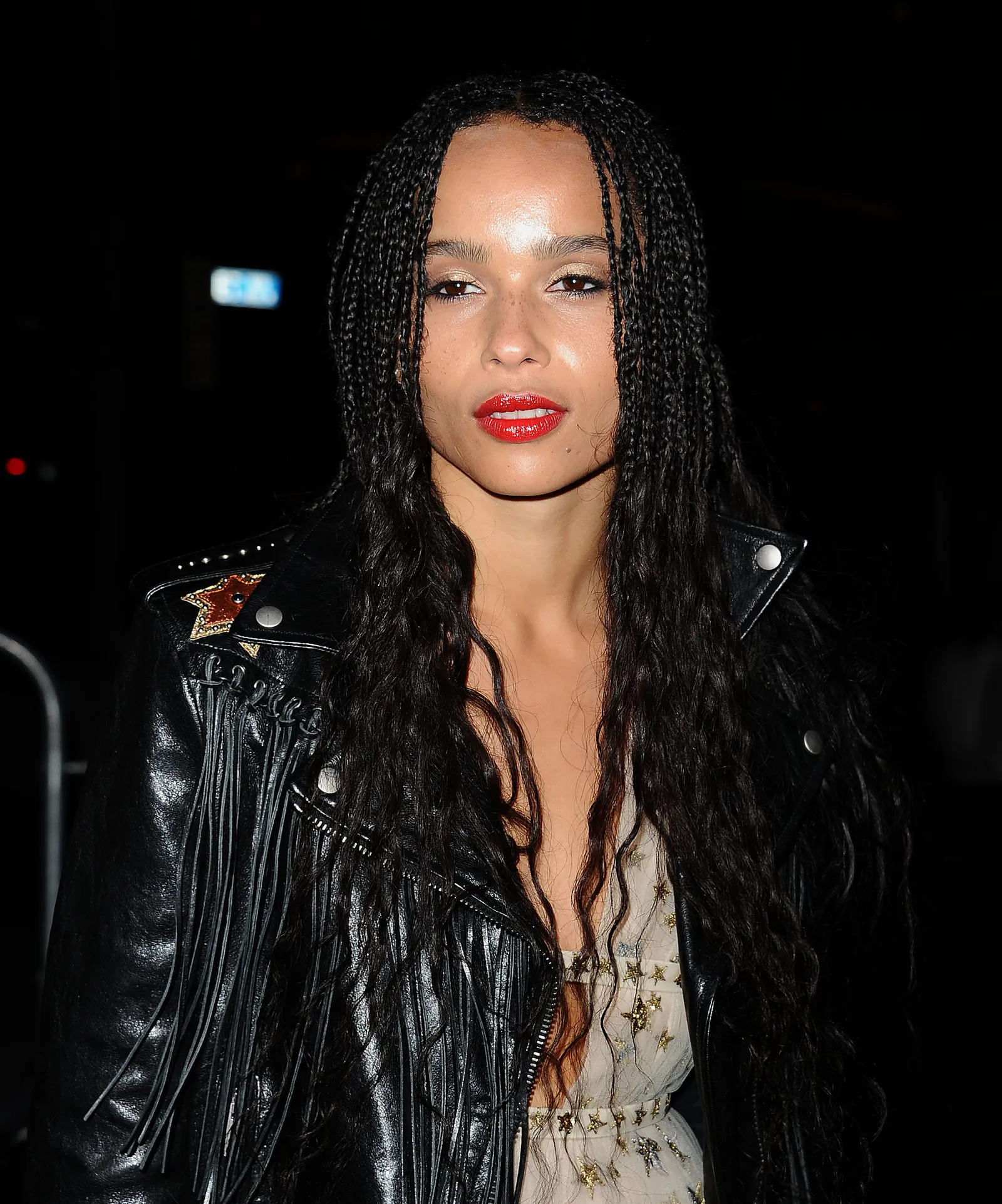 Zoe Kravitz w boho fryzurze, czarnej skórzanej kurtce, z wyrazistymi ustami w czerwonej szmince.