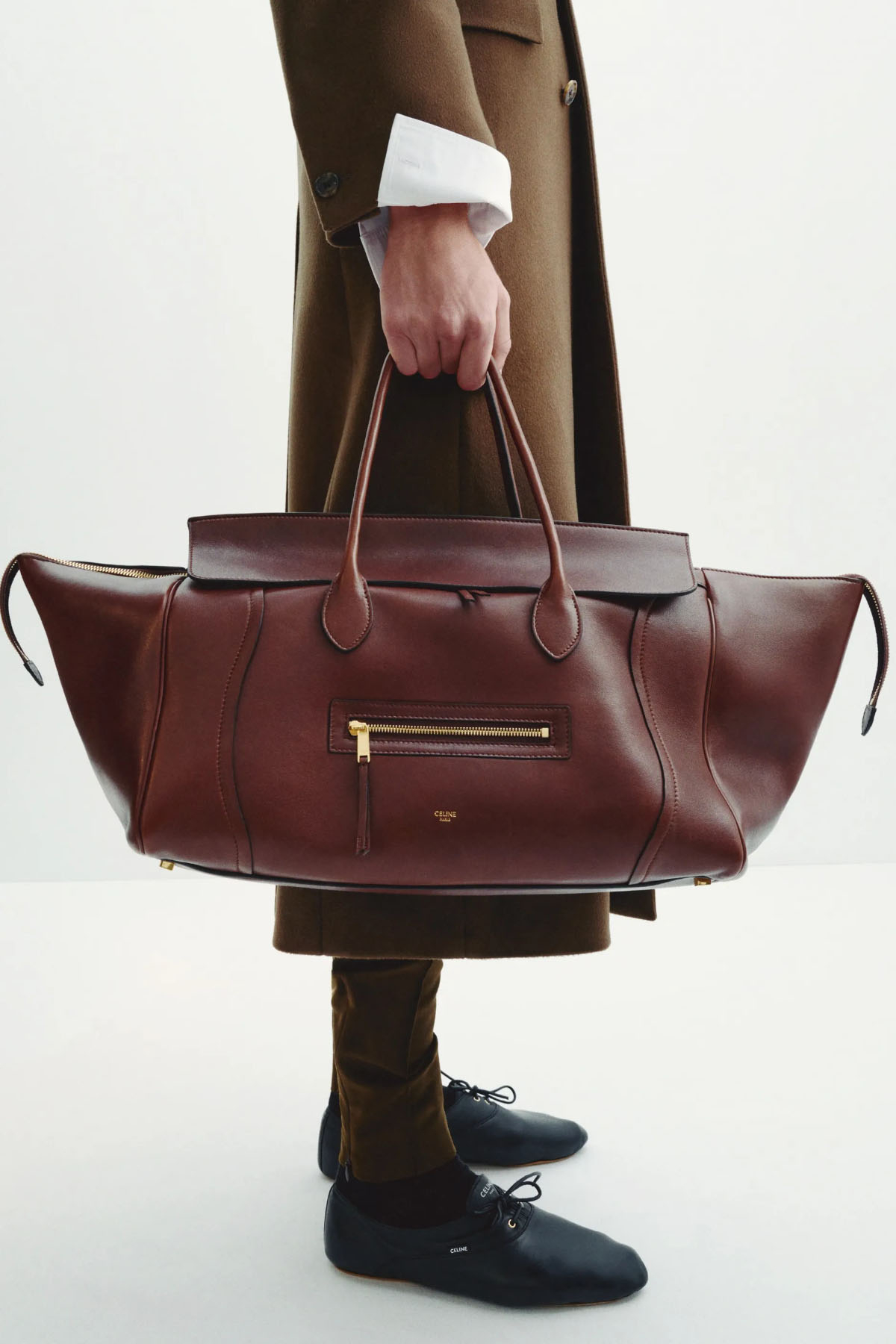 Nowa it-bag Celine w kolorze brązowym, trzymana przez osobę w eleganckim płaszczu i czarnych butach.
