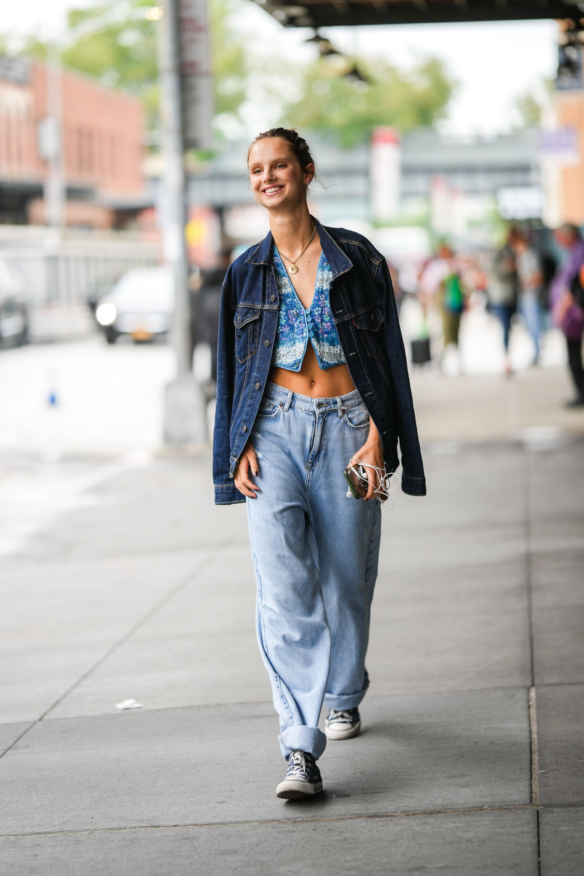 Kobieta spacerująca po ulicy, ubrana w cropped jeans oraz trampki, z uśmiechem na twarzy.