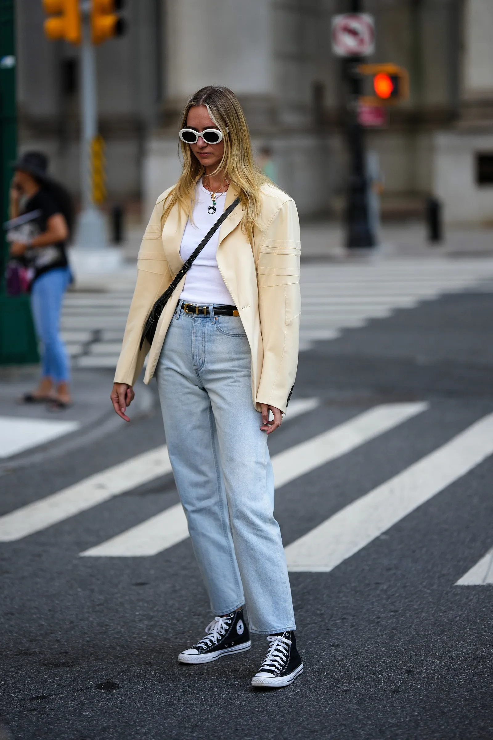 Kobieta w białej marynarce i białym t-shircie, nosząca cropped jeans i trampki.