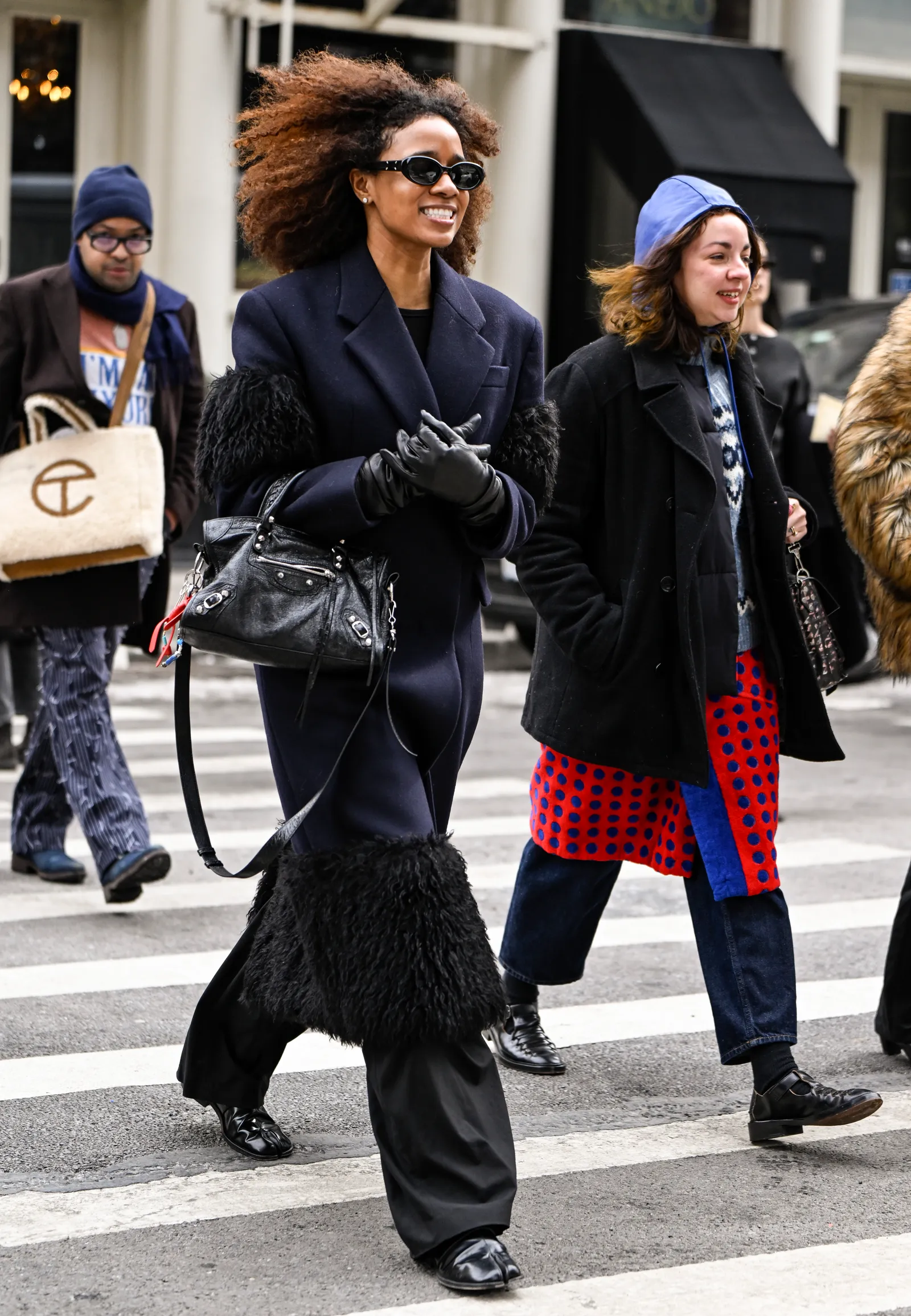 Stylowa kobieta w granatowym płaszczu na zimę 2025, ozdobionym futrem, idzie ulicą w towarzystwie przyjaciół.