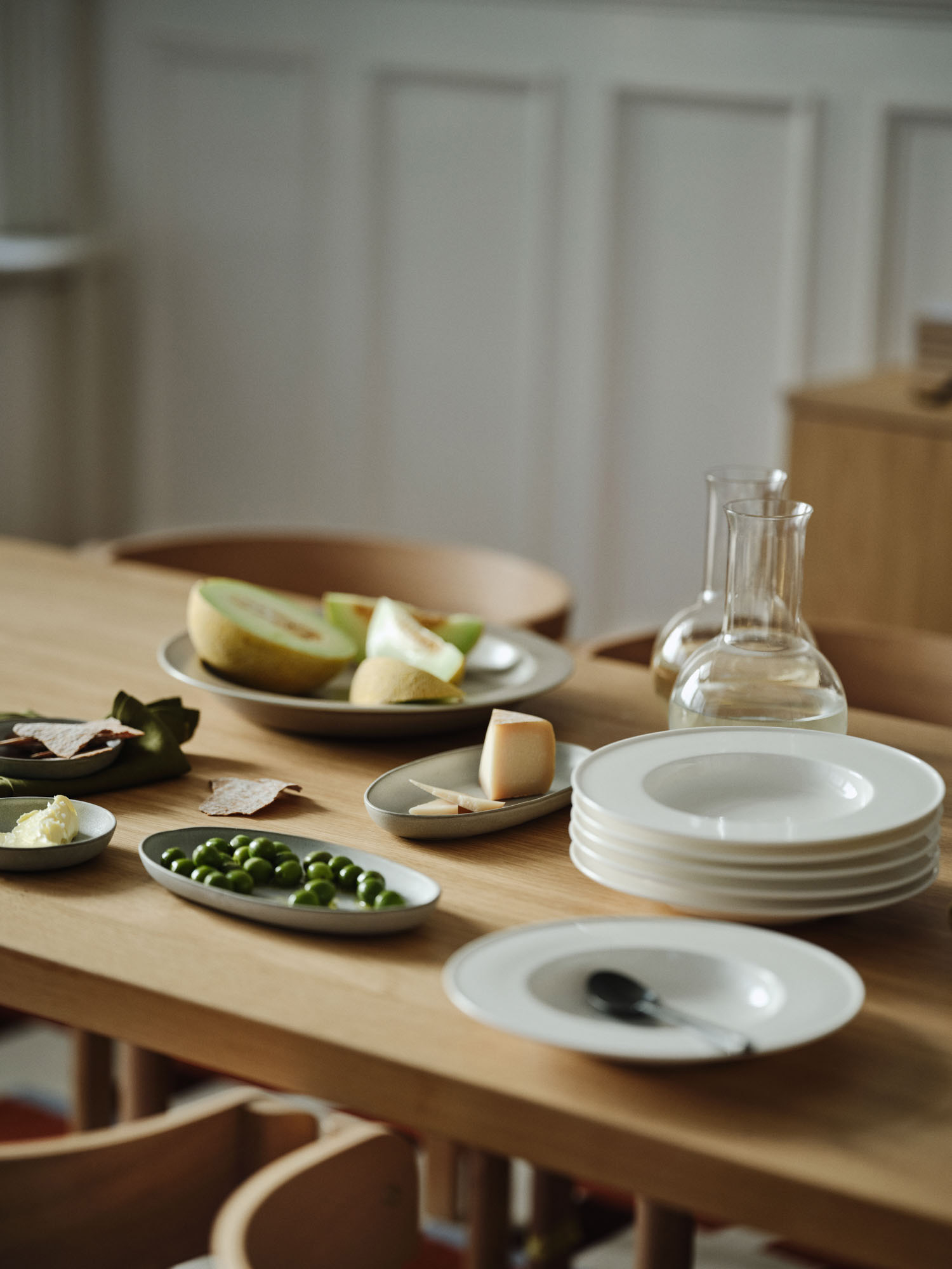 Na stole Ikea znajdują się talerze, owoce, oliwki i dzbanek z wodą, tworząc przytulną atmosferę posiłku.
