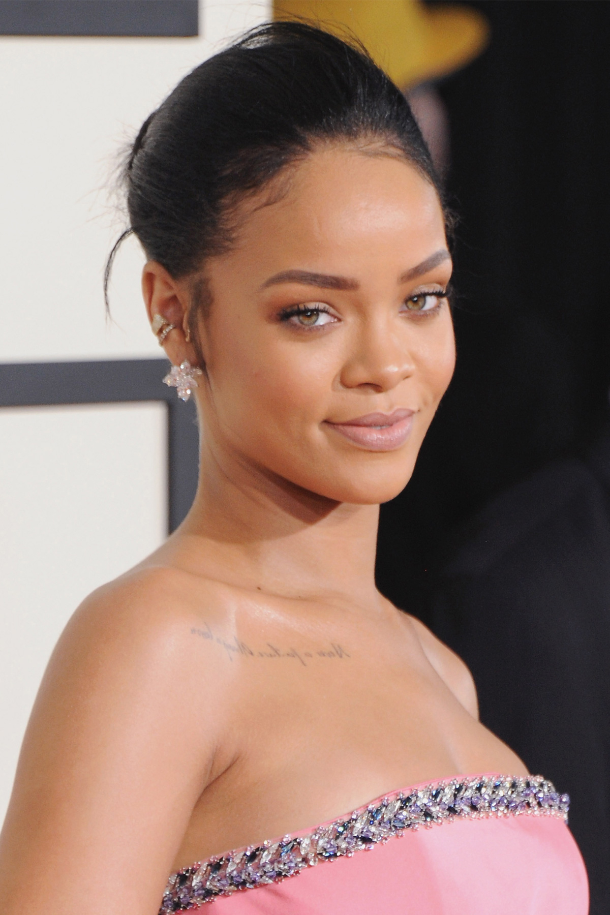 Rihanna w różowej sukni bez ramiączek z wyszywanym dekoltem, z włosami spiętymi w kok i delikatnym makijażem.