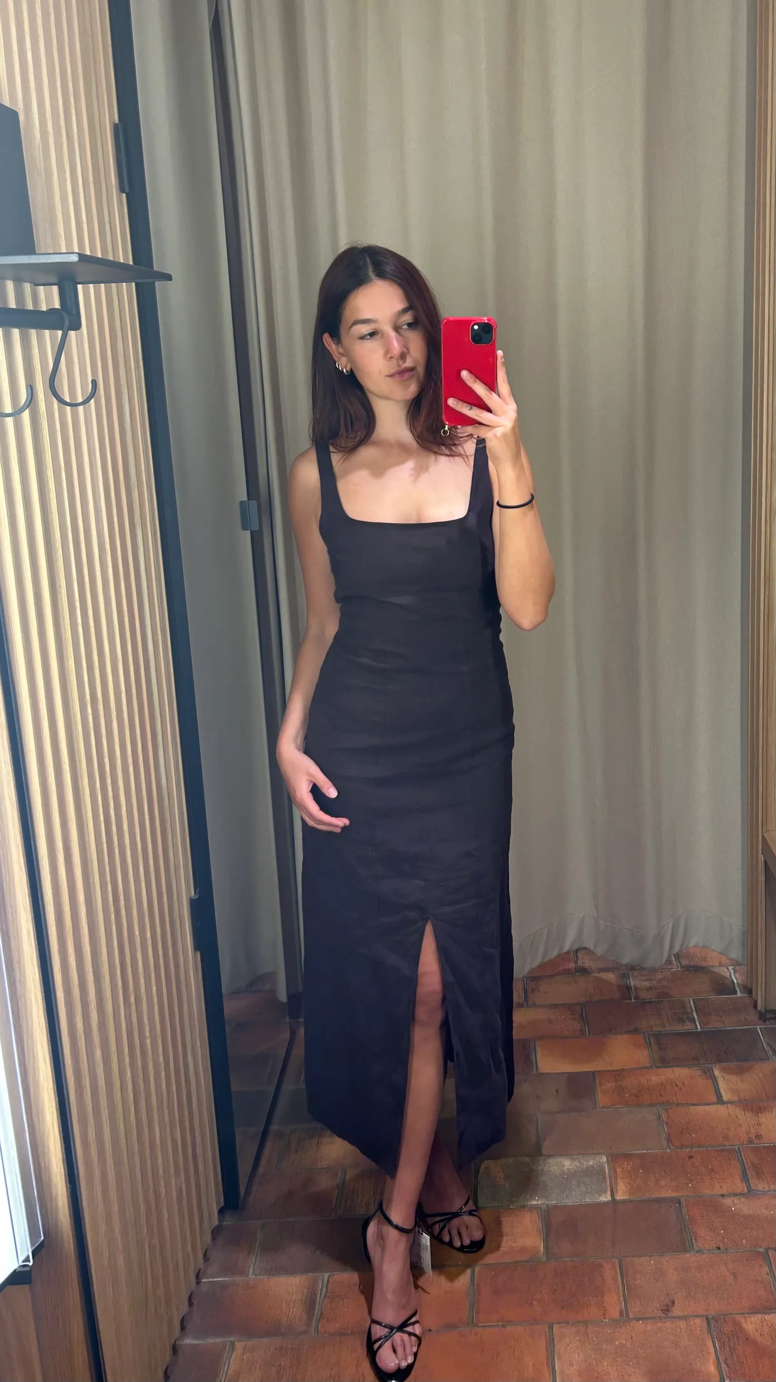 Stylowa sukienka na wesele w kolorze czarnym, z dekoltem w serek i rozcięciem na nogę. Modelka trzyma telefon w dłoni.
