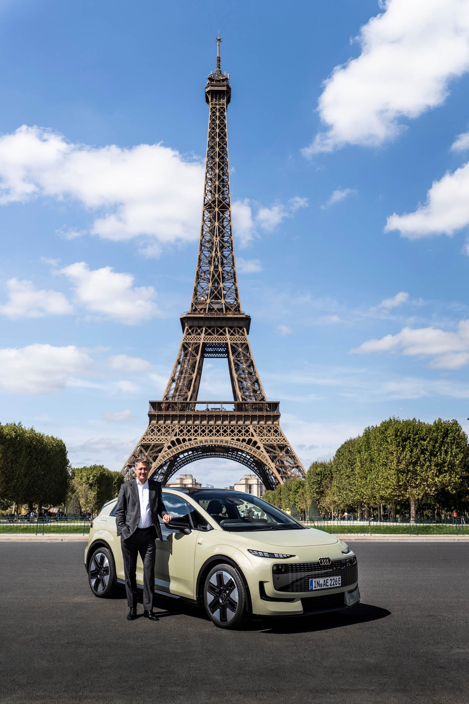 CEO Audi, Gernot D&ouml;llner stoi obok nowego modelu Audi A2 e-tron przed Wieżą Eiffla w Paryżu, w tle błękitne niebo i zieleń.