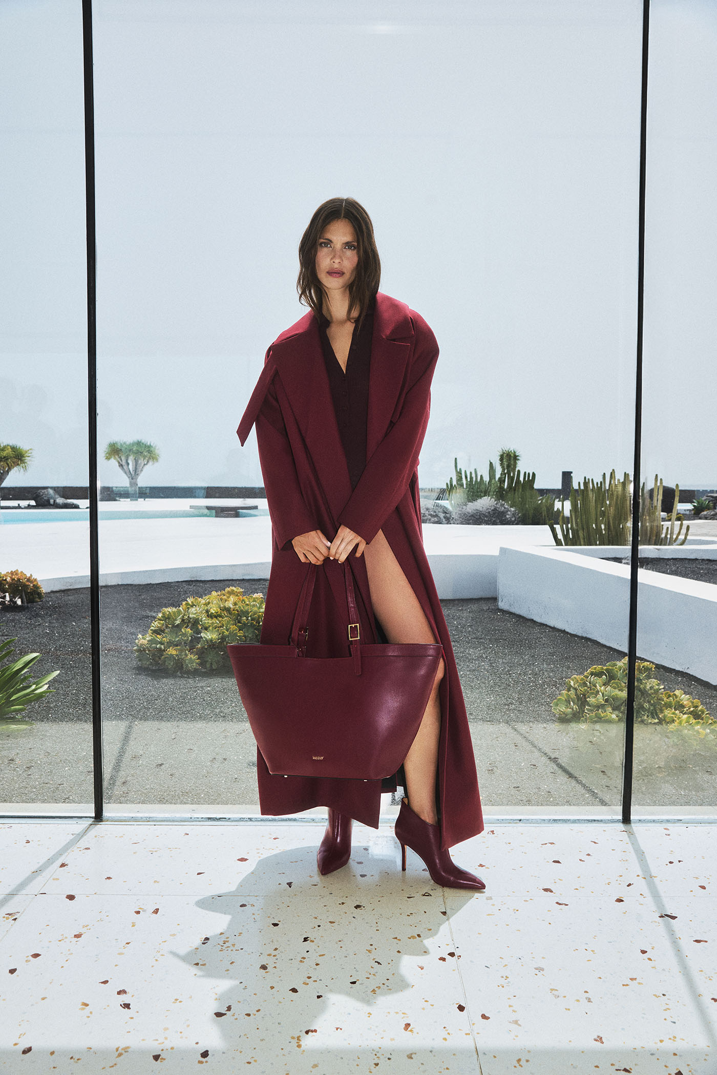 Modelka w burgundowym płaszczu, z torebką i butami z kolekcji Ruby Tones marki Kazar.
