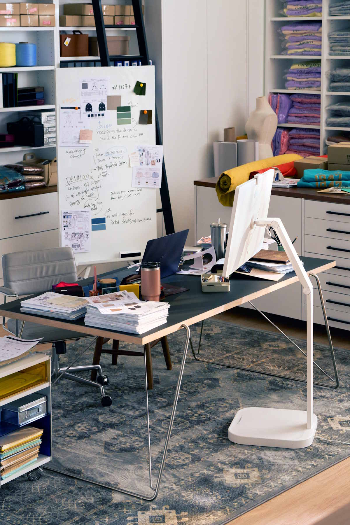 Biuro z dużym biurkiem, laptopem, notatkami oraz różnymi materiałami, zorganizowane na tle kolorowych tkanin. LG Smart Monitor Swing.