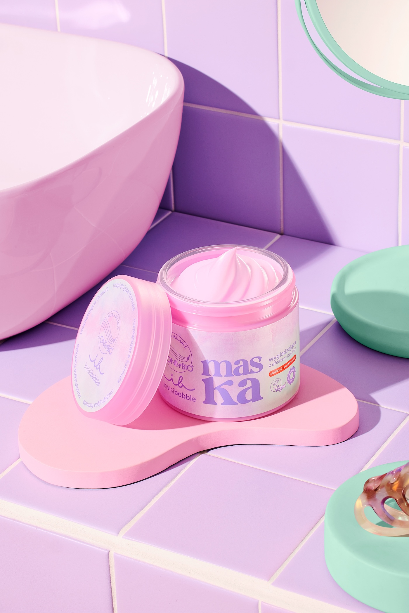 Maska wygładzająca z efektem bouncy hair OnlyBio x invisibobble, w tle fioletowe płytki łazienkowe, seledynowe i różowe podstwki.