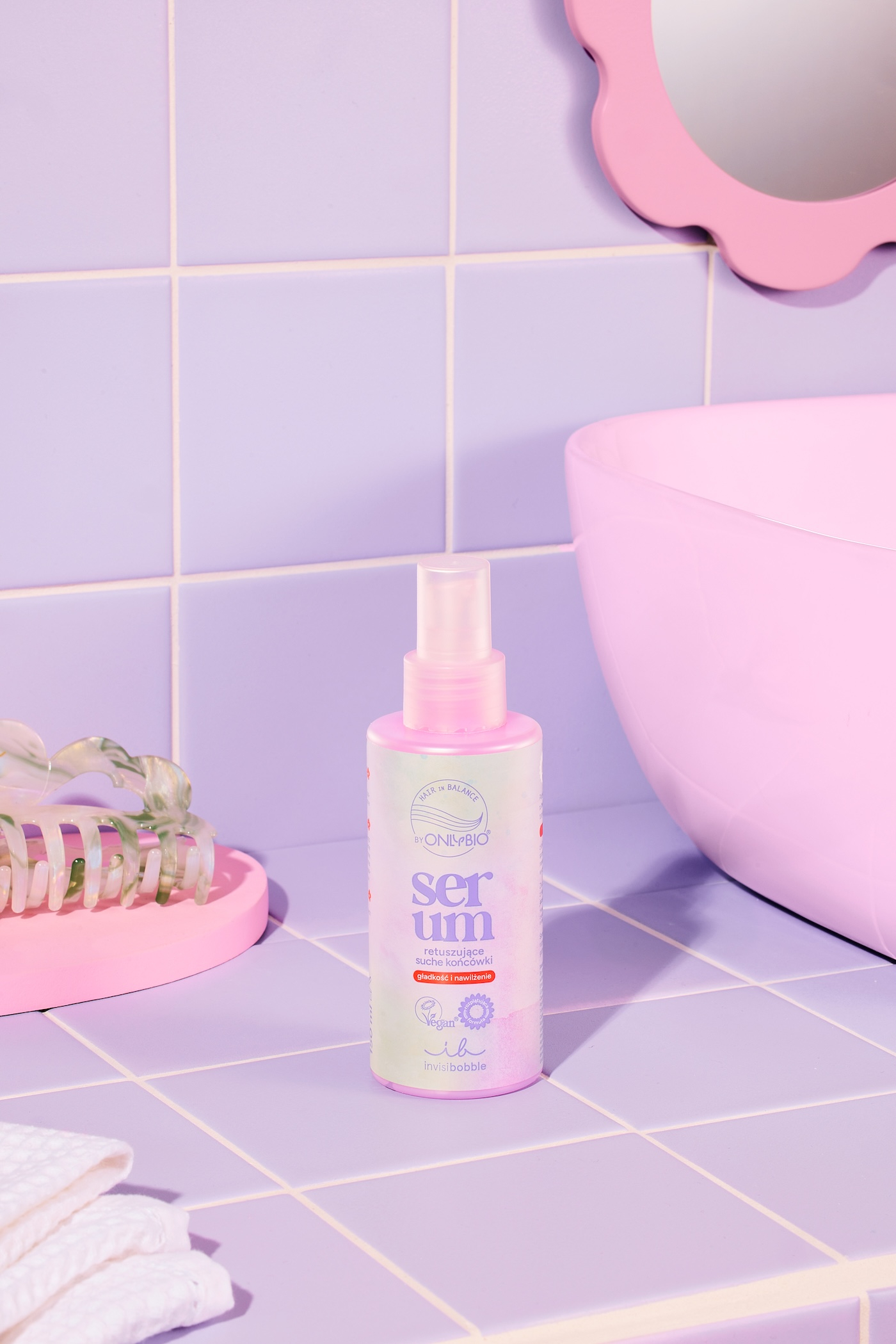 Serum retuszujące suche końcówki OnlyBio x invisibobble, w tle fioletowe płytki łazienkowe, ręcznik oraz dekoracja.