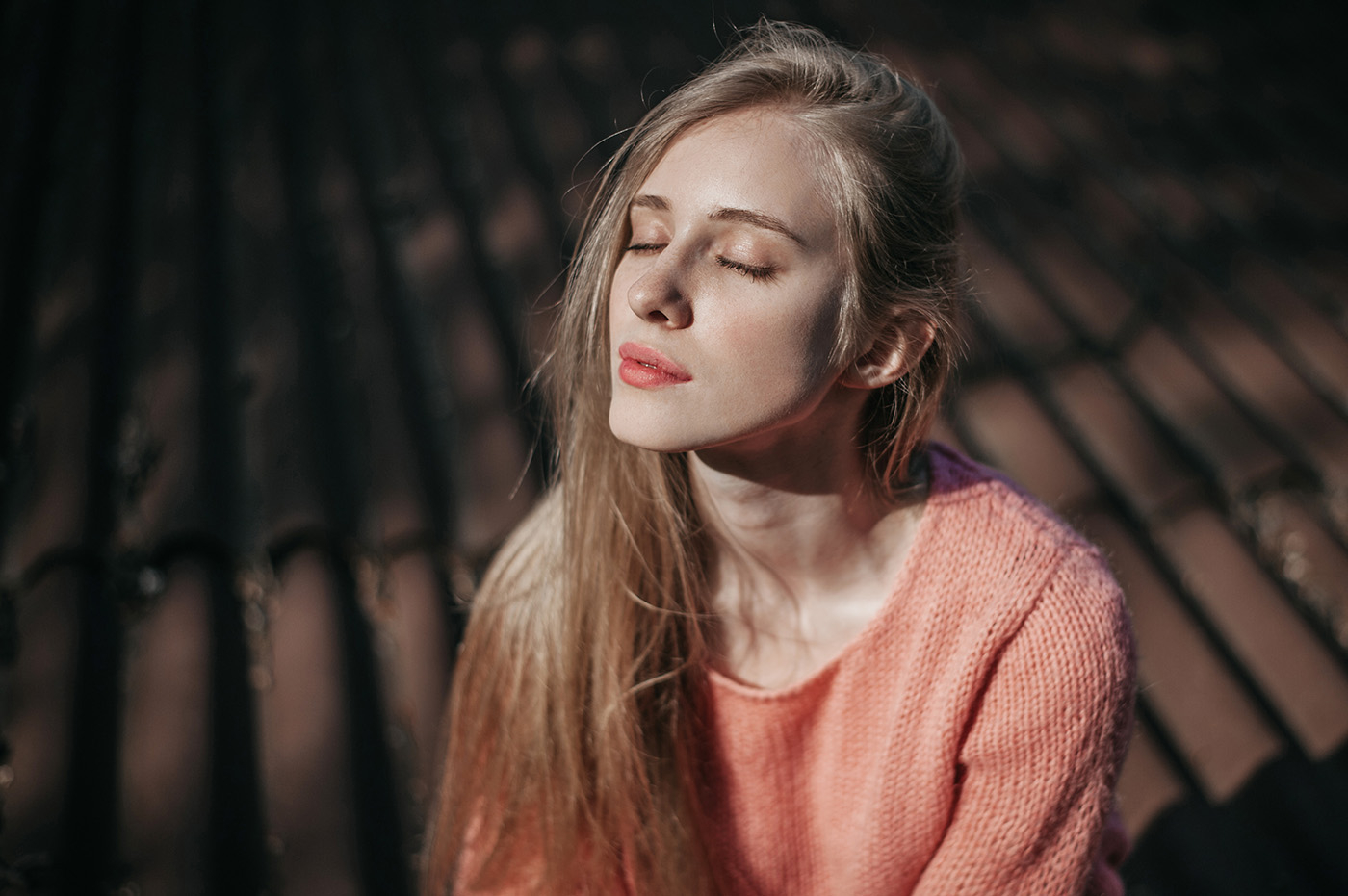 Modelka siedząca na drewnianym pomoście, ma długie blond włosy i sweter w kolorze brzoskwiniowym.