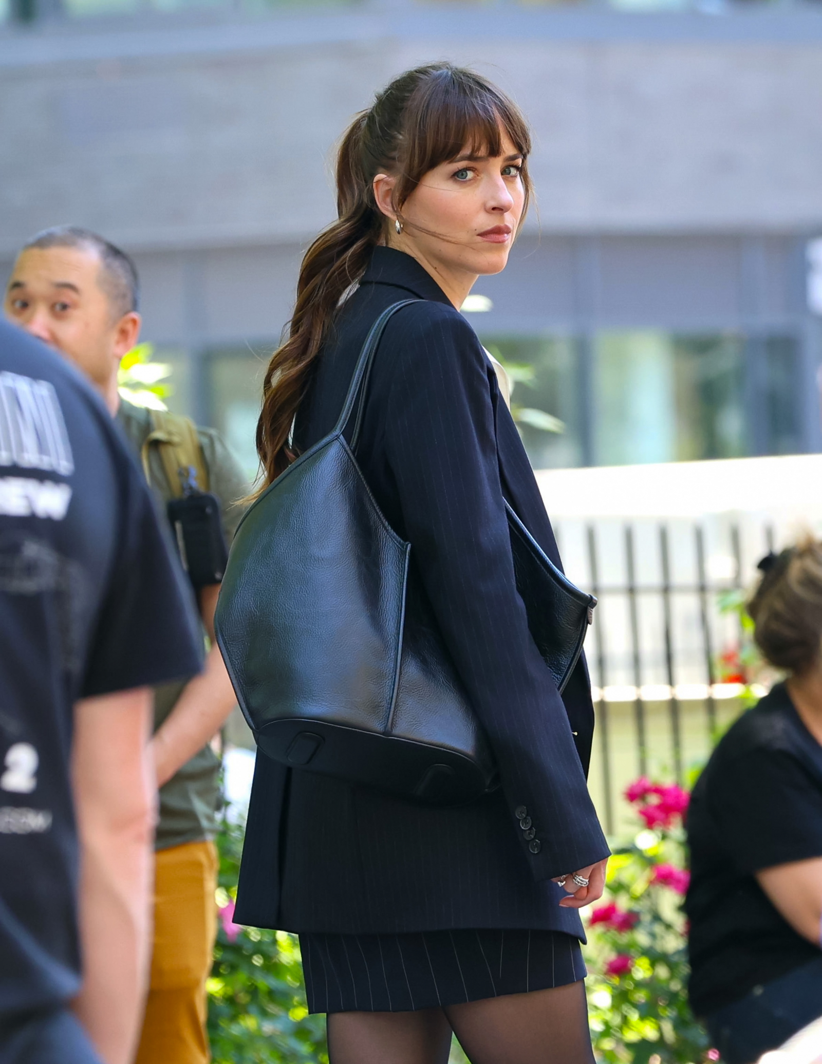 Dakota Johnson w eleganckim zestawie, z czarną torebką skórzaną Hereu Calella na ramieniu, patrzy w stronę obiektywu.