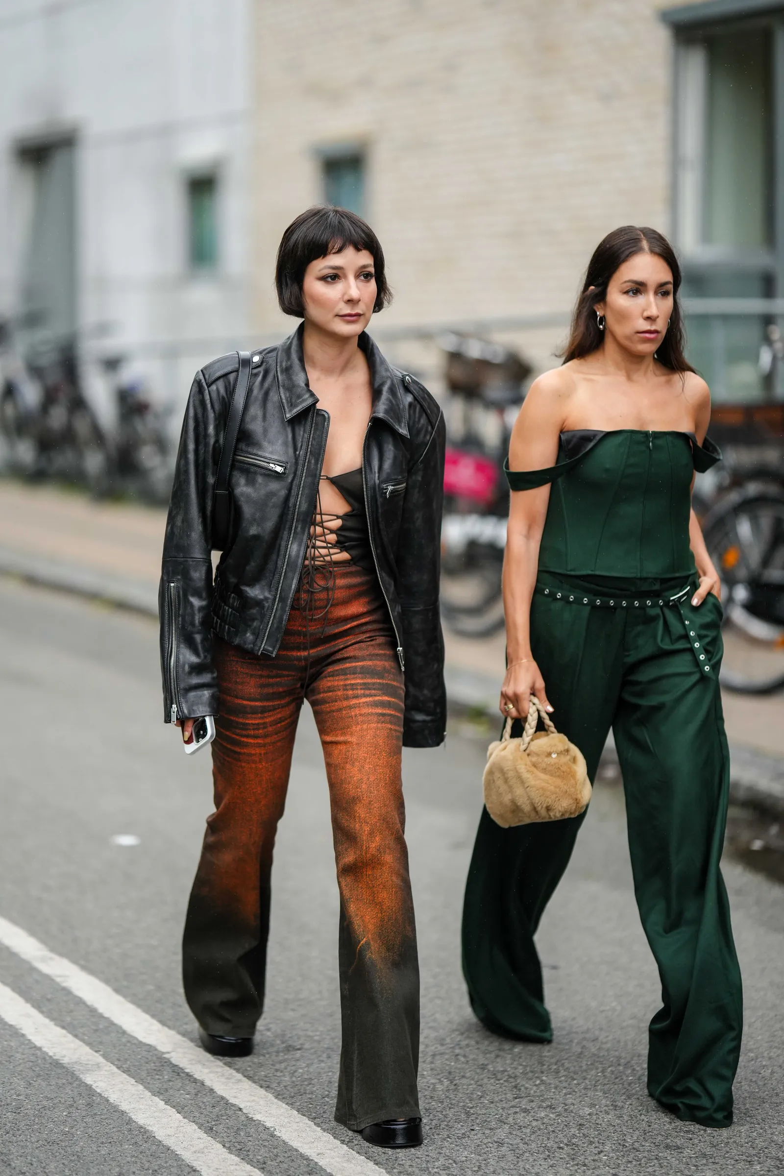 Modelka w brązowo-pomarańczowych jeansach dzwonach w stylu lat 70. oraz botkach typu biker przechadza się ulicą.