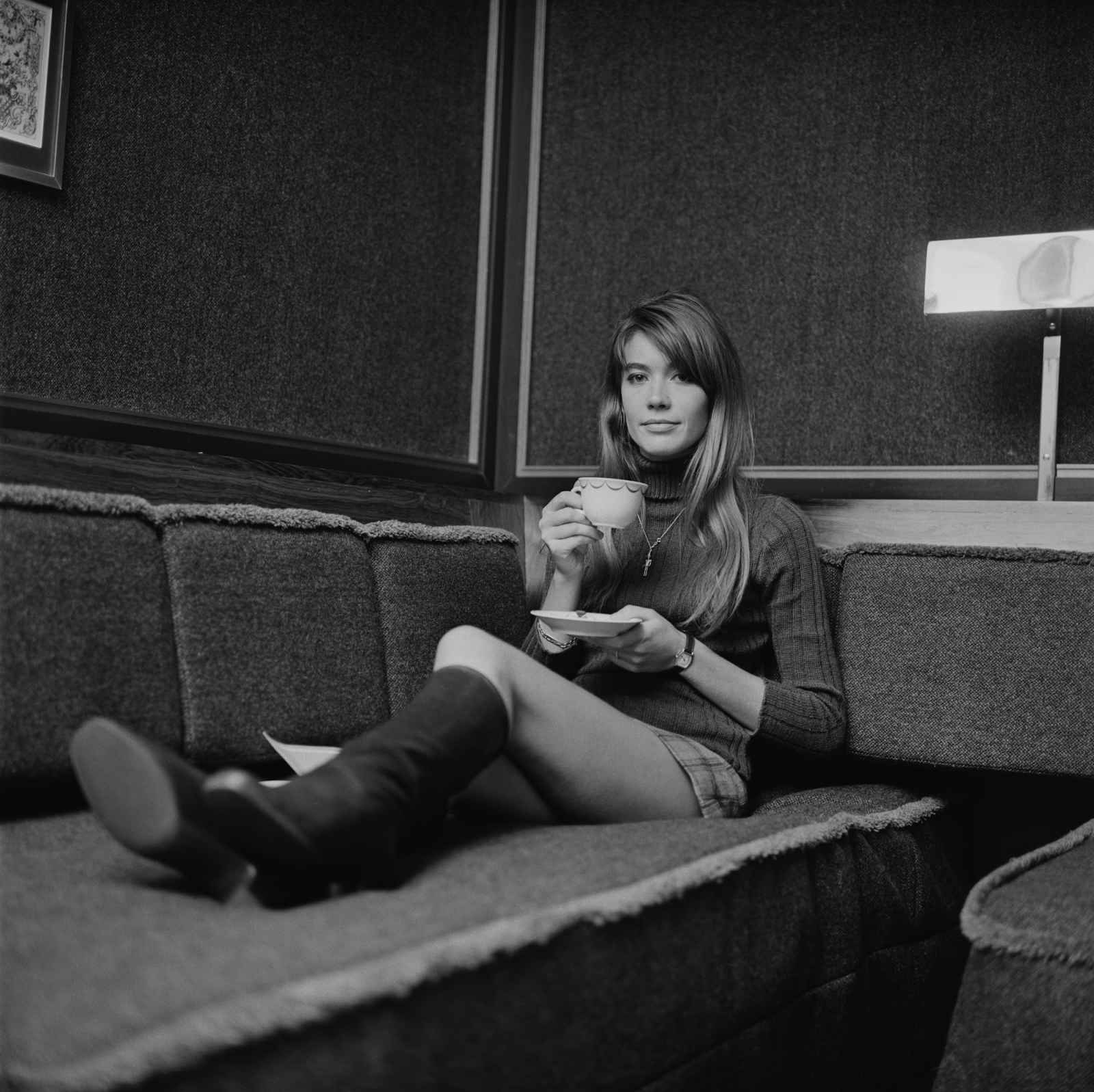 Françoise Hardy w krótkiej spódnicy, brązowe kozaki na obcasie, relaksuje się z filiżanką herbaty na sofie.