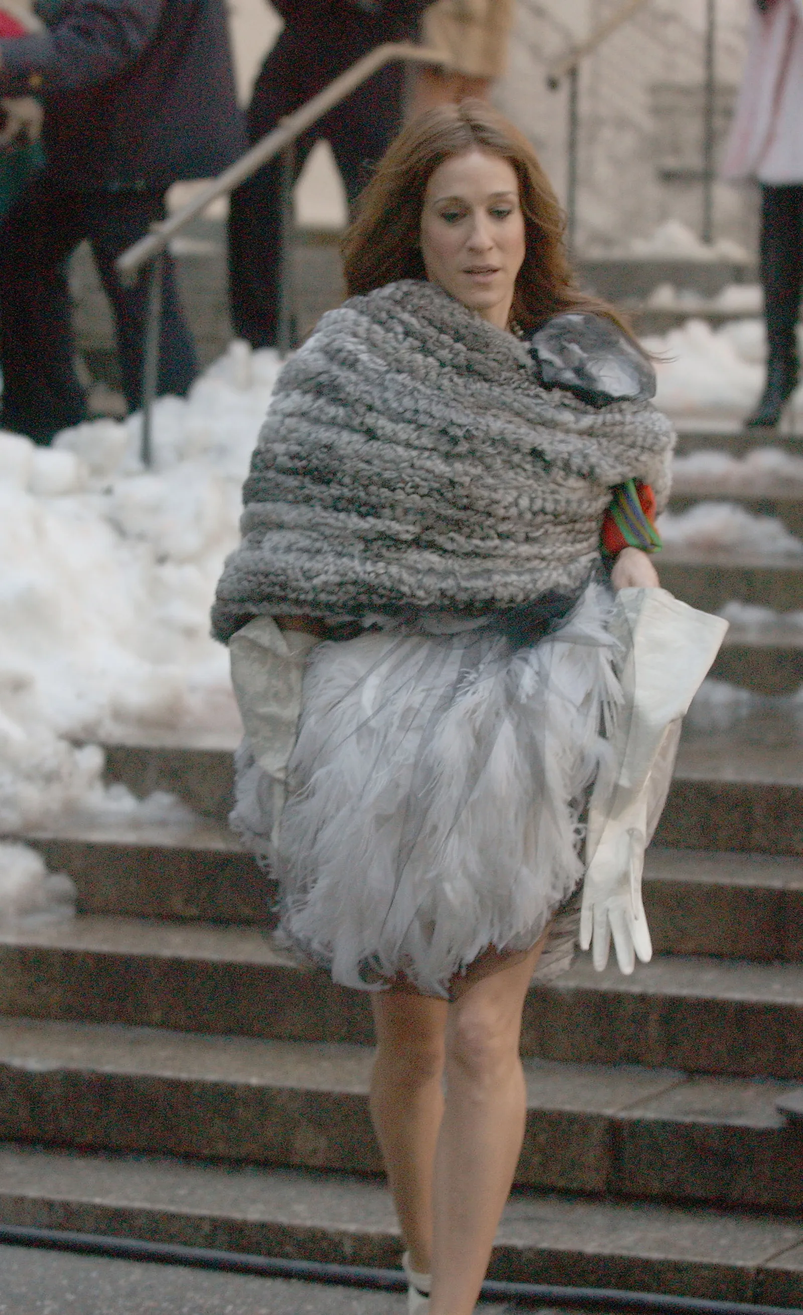 Sarah Jessica Parker jako Carrie Bradshaw, ubrana w futrzany szal i tiulową spódnicę, idzie po schodach.
