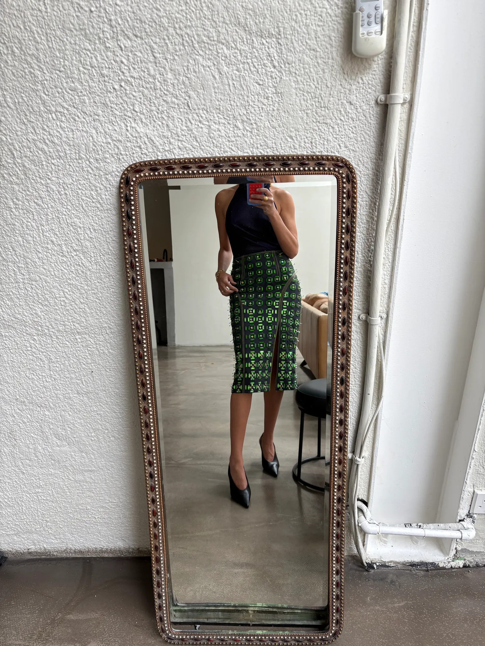 Kobieta w zielonej spódnicy z wzorem w lustrze, z czarną bluzką i eleganckimi szpilkami.