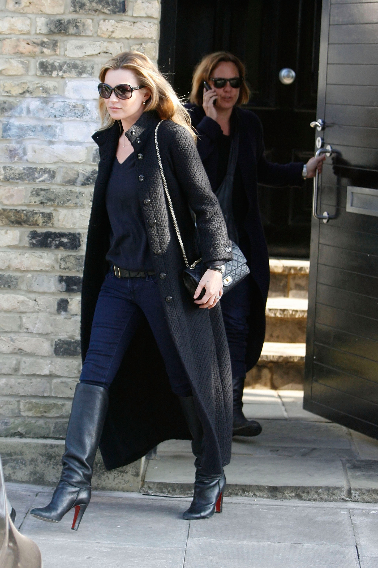 Kate Moss w granatowych skinny jeans, czarnych skórzanych kozaczkach na obcasie, wychodzi z budynku.