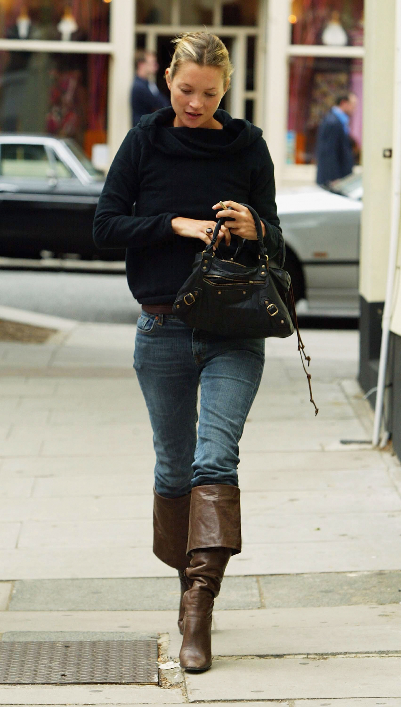 Kate Moss w czarnej bluzie, niebieskich skinny jeans oraz brązowych kozakach z wywiniętą cholewką.