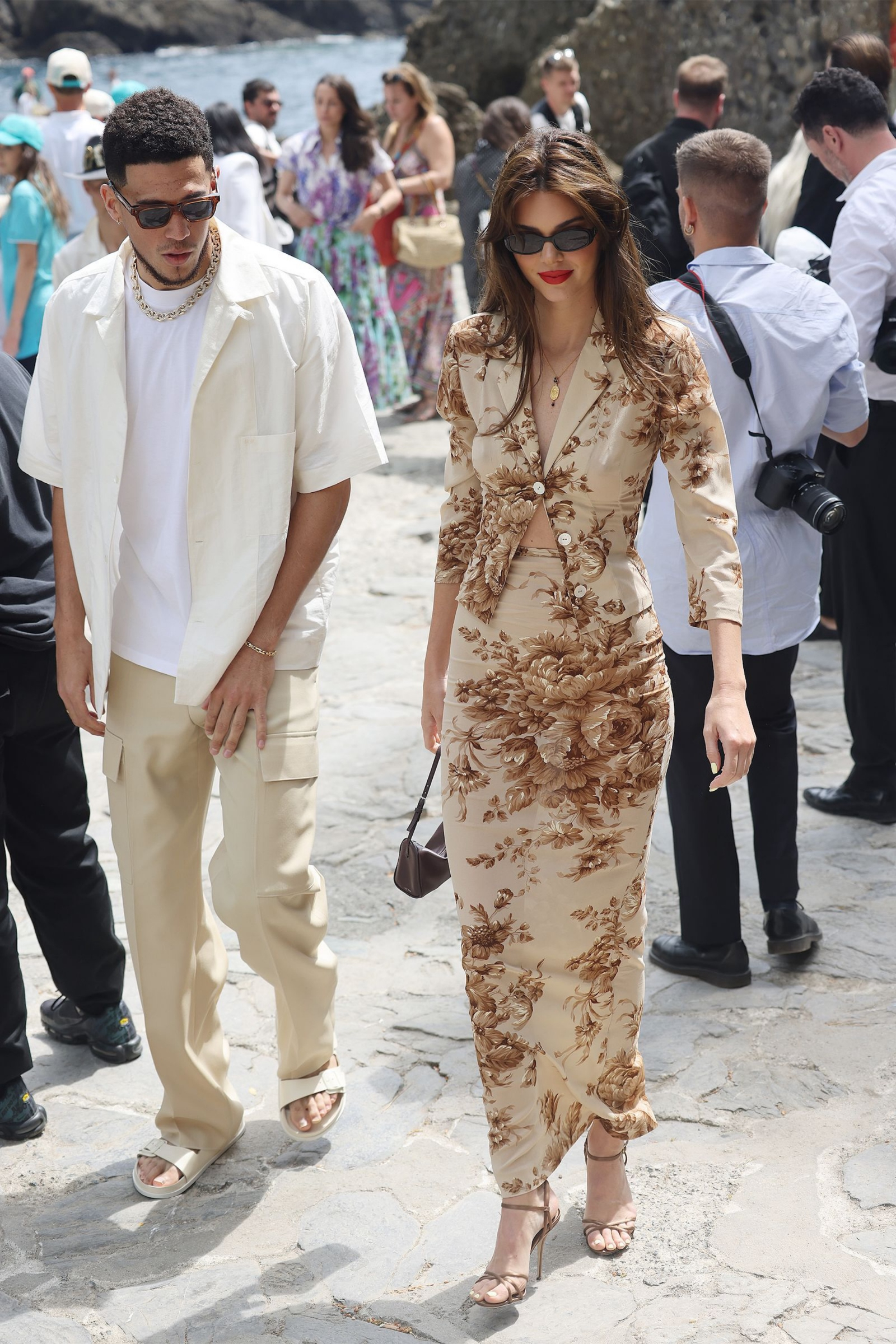 Kendall Jenner w eleganckiej koszuli damskiej i długiej spódnicy w kwiaty, spaceruje wśród ludzi.