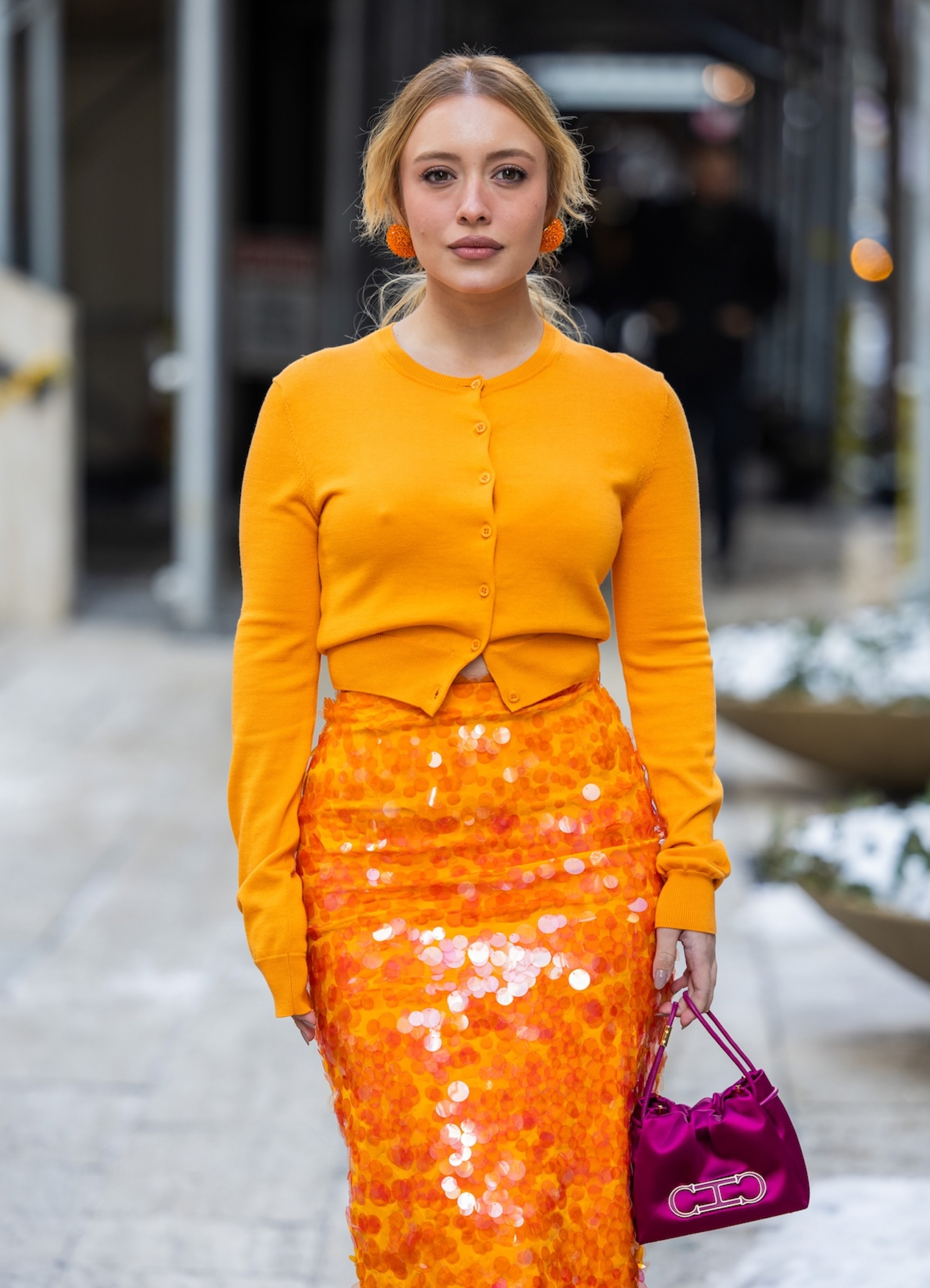 Kobieta w pomarańczowym kardiganie i pomarańczowej spódnicy cekinowej midi Carolina Herrera, trzymająca różową torebkę.
