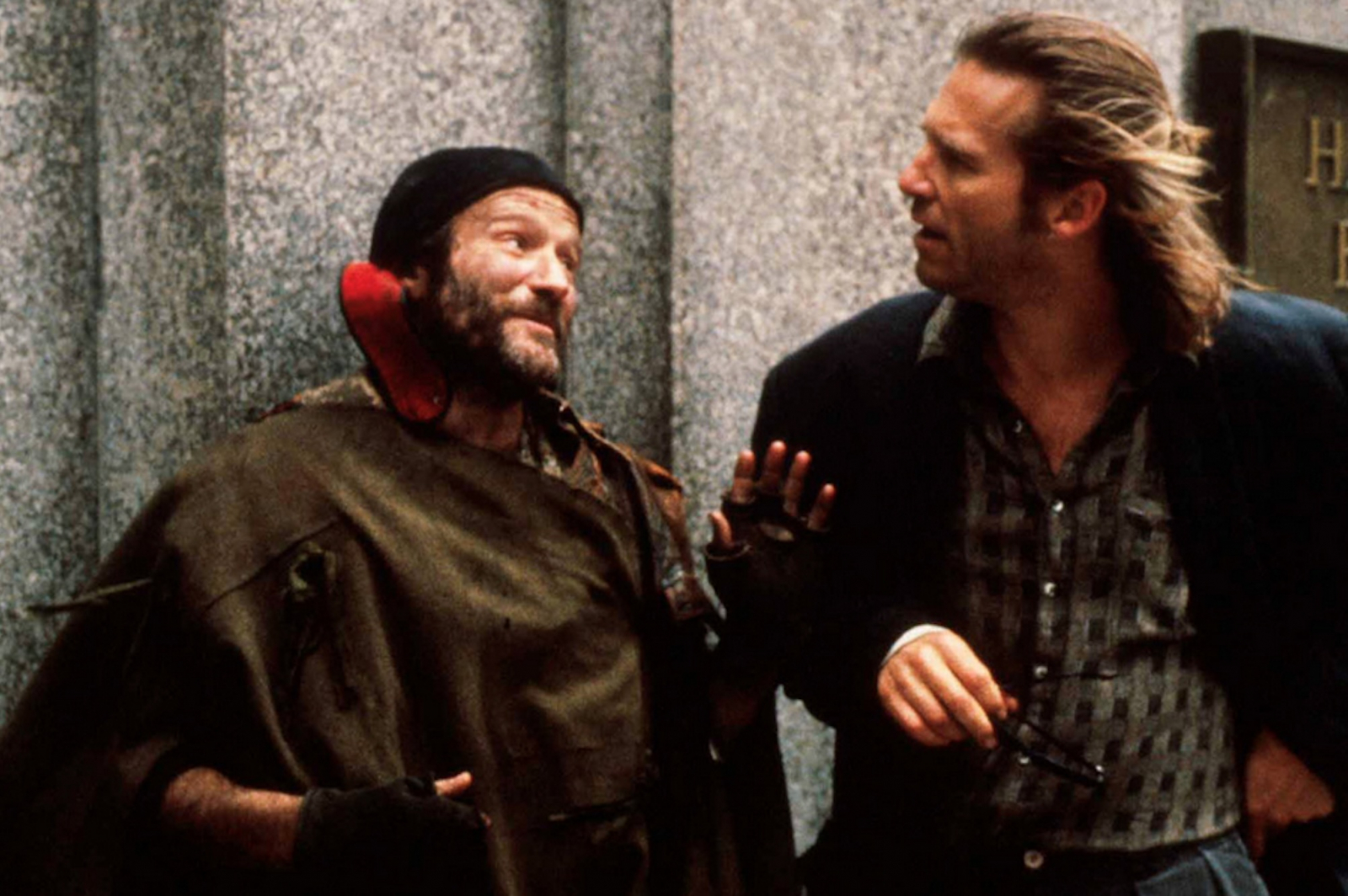 Robin Williams w filmie „Fisher King” rozmawia z mężczyzną w eleganckim stroju, ukazując emocjonalny moment ich interakcji.