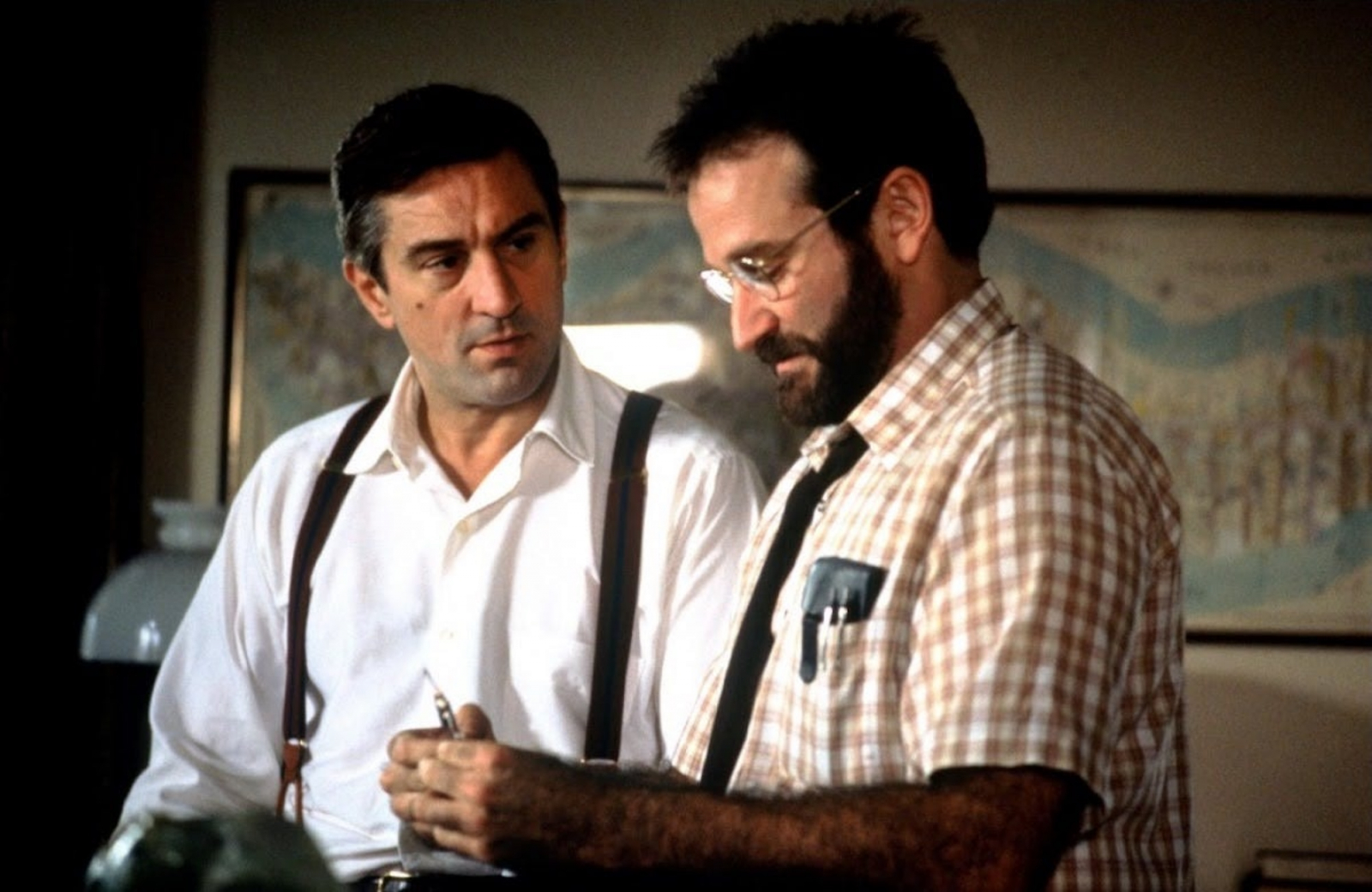 Robert De Niro i Robin Williams w filmie „Przebudzenia”, rozmawiając w pokoju, z dokumentami w rękach.