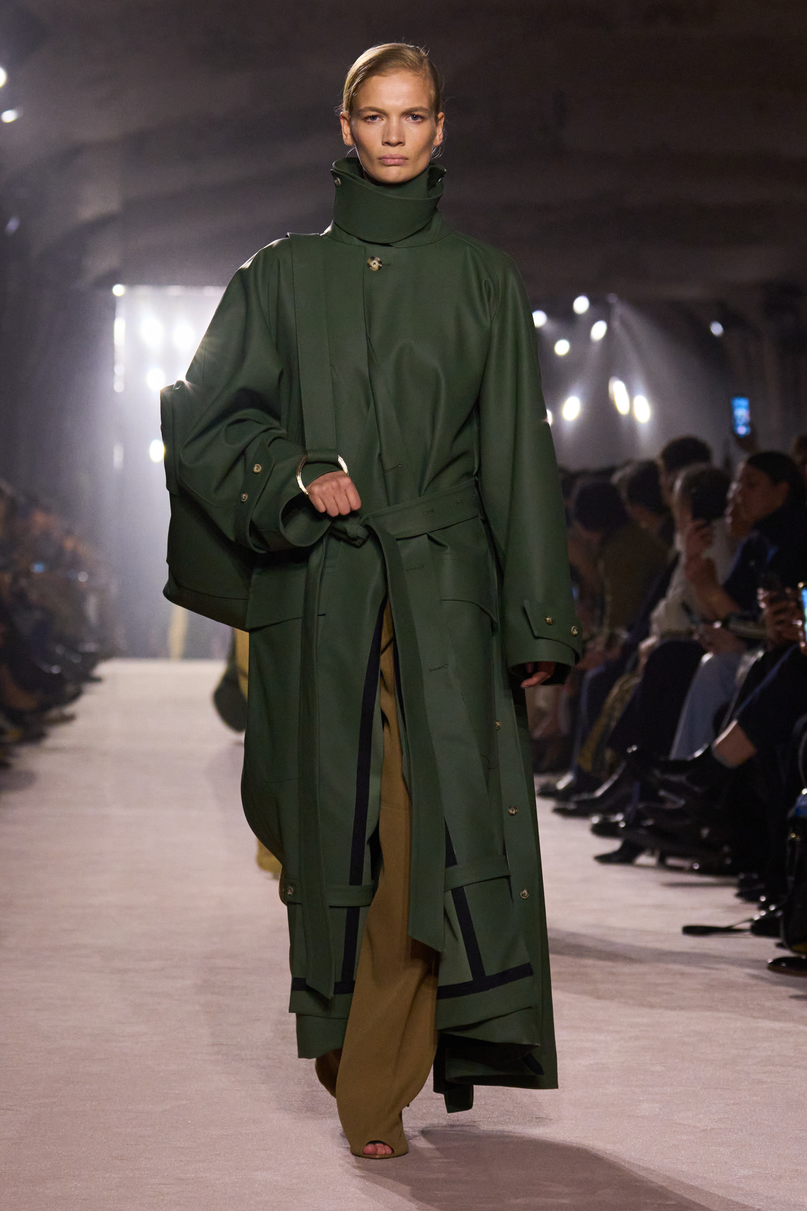 Zielony trencz od Victorii Beckham na sezon jesień-zima 2025-2026, modelka na wybiegu w eleganckiej stylizacji.