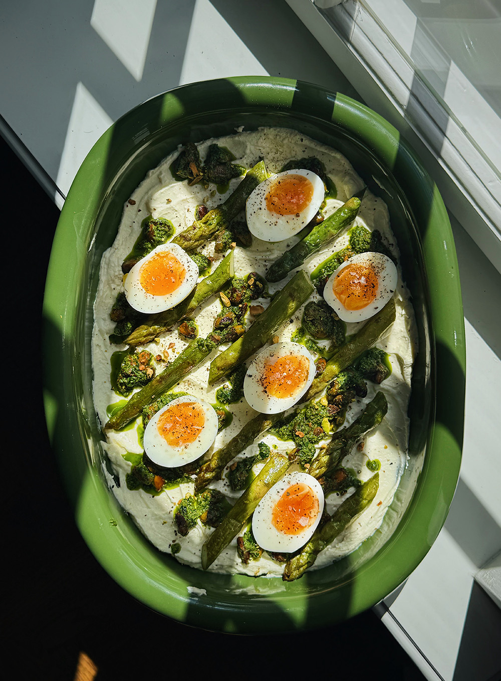 Zielona forma z nakładką z kremowego sosu, jajek na twardo, zielonego asparagusa i pesto, pod światło.