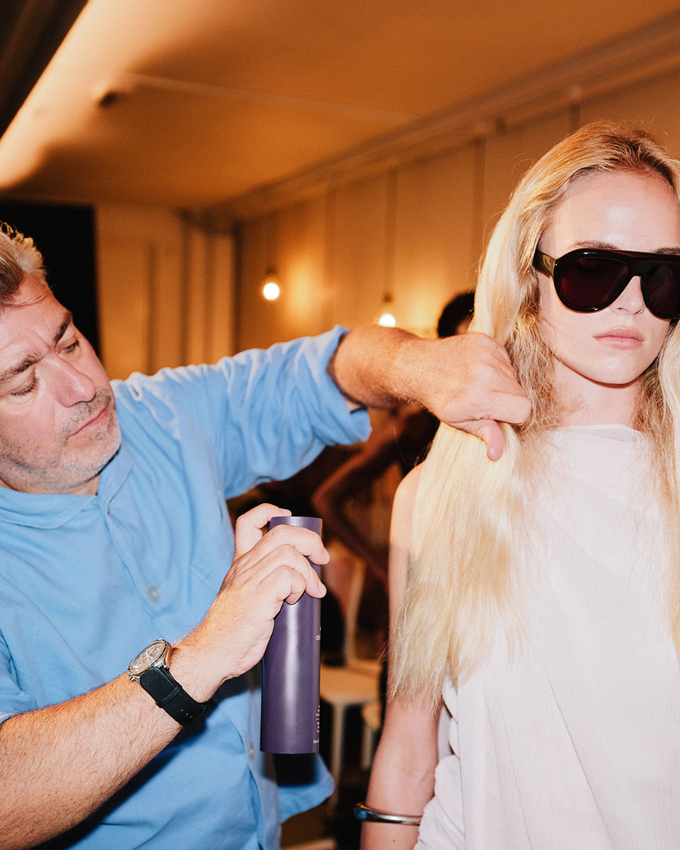 Stylista fryzur rozpyla lakier do włosów na modelce o blond włosach
