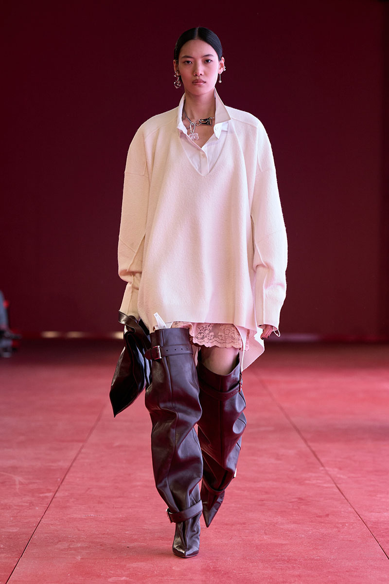 Modelka prezentuje elegancką stylizację H&M, składającą się z oversize'owego swetra i długich, skórzanych butów.
