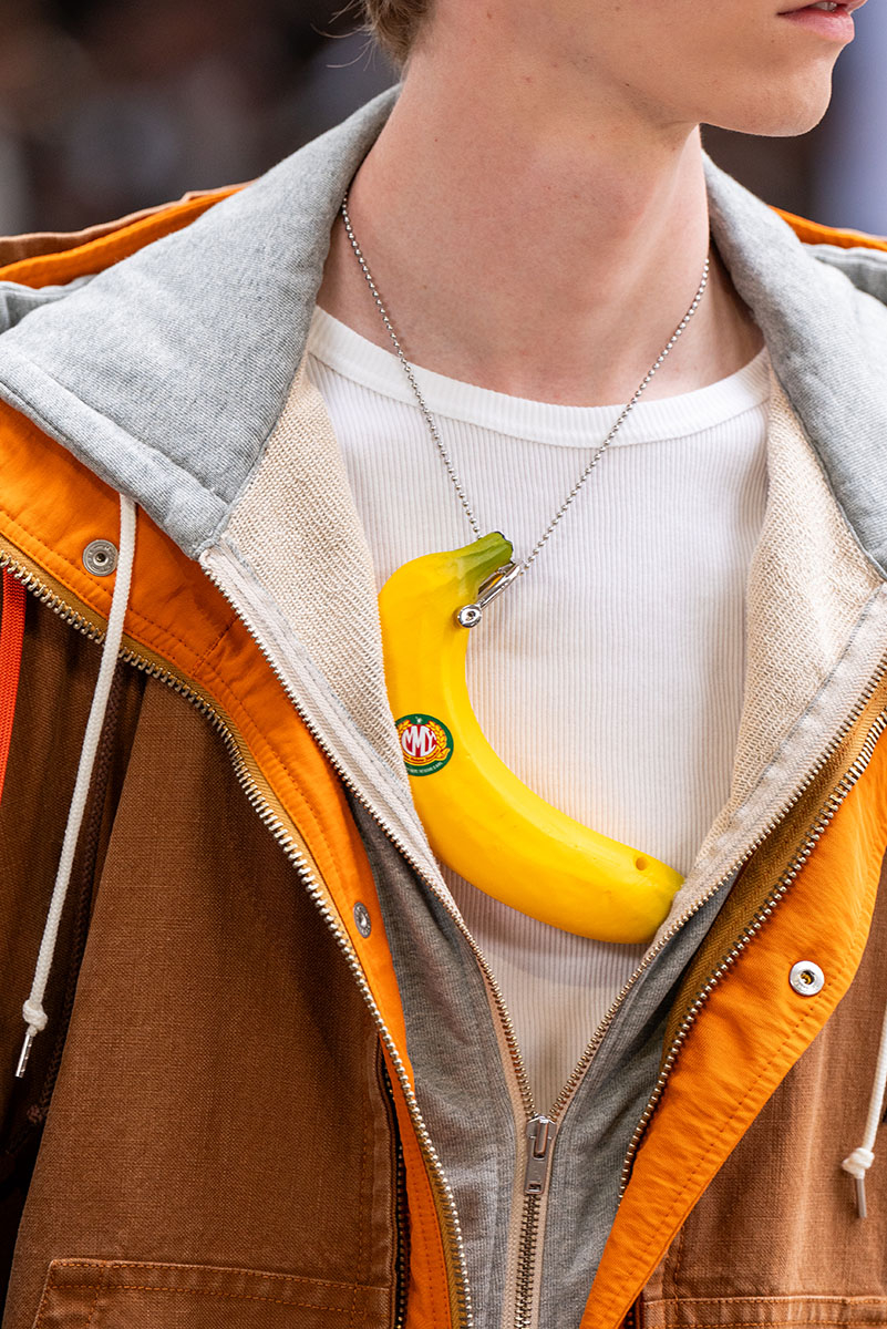Mężczyzna w oryginalnej stylizacji na wiosnę-lato 2026, z naszyjnikiem w kształcie banana i modną kurtką.