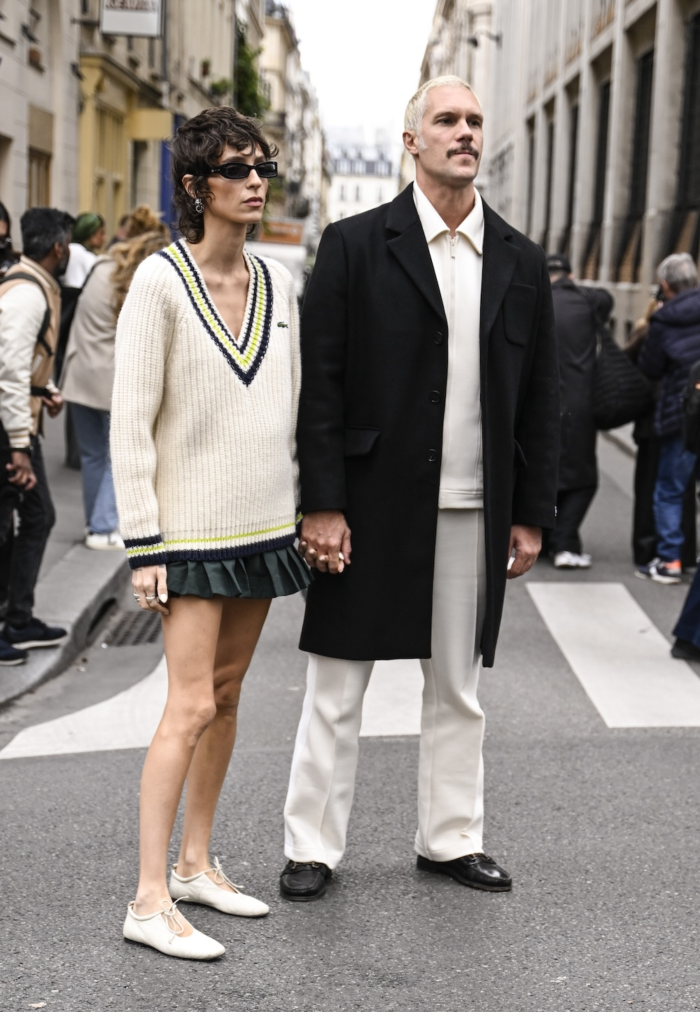 Dama w eleganckim swetrze damskim oversize i plisowanej spódnicy mini, trzymająca się za ręce z mężczyzną w eleganckim płaszczu.
